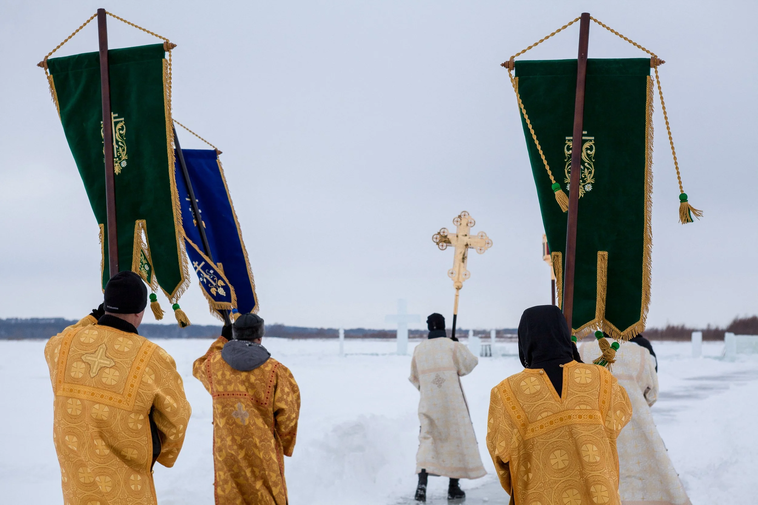 Groupe de personnes vêtues de robes de cérémonie en or et portant des bannières et une croix à l'extérieur dans un paysage enneigé en Russie.