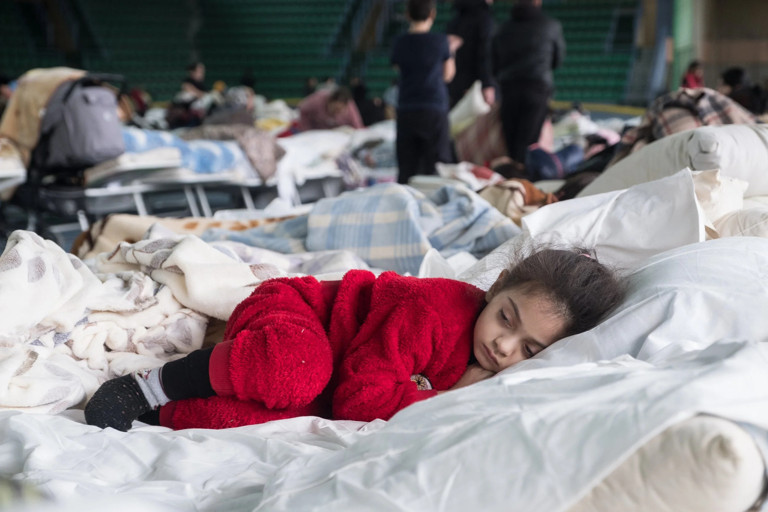 Une fillette ukrainienne dort sur un matelas dans un centre d'accueil bondé avec d'autres personnes et matelas en arrière-plan à Chisinau en Moldavie.