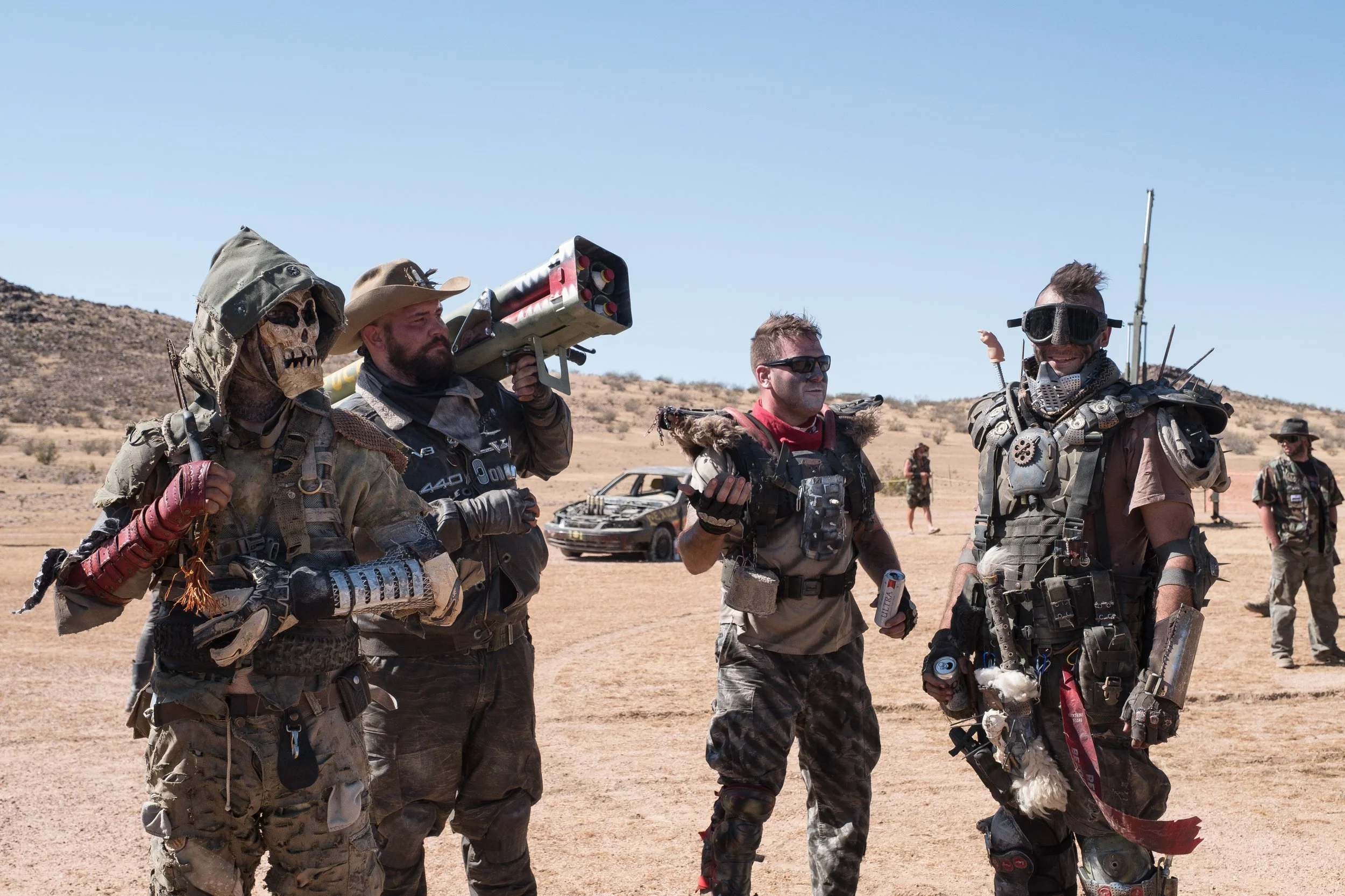 Groupe de personnes déguisées en personnages de science-fiction ou post-apocalyptiques dans un désert, équipées de costumes élaborés avec des accessoires et des armements légers à Wasteland.