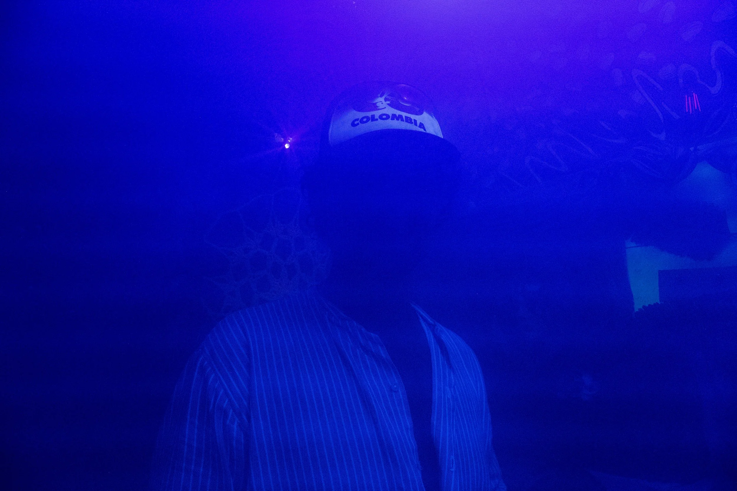 Personne portant une casquette avec inscription "Colombia" dans un environnement sombre avec un éclairage bleu