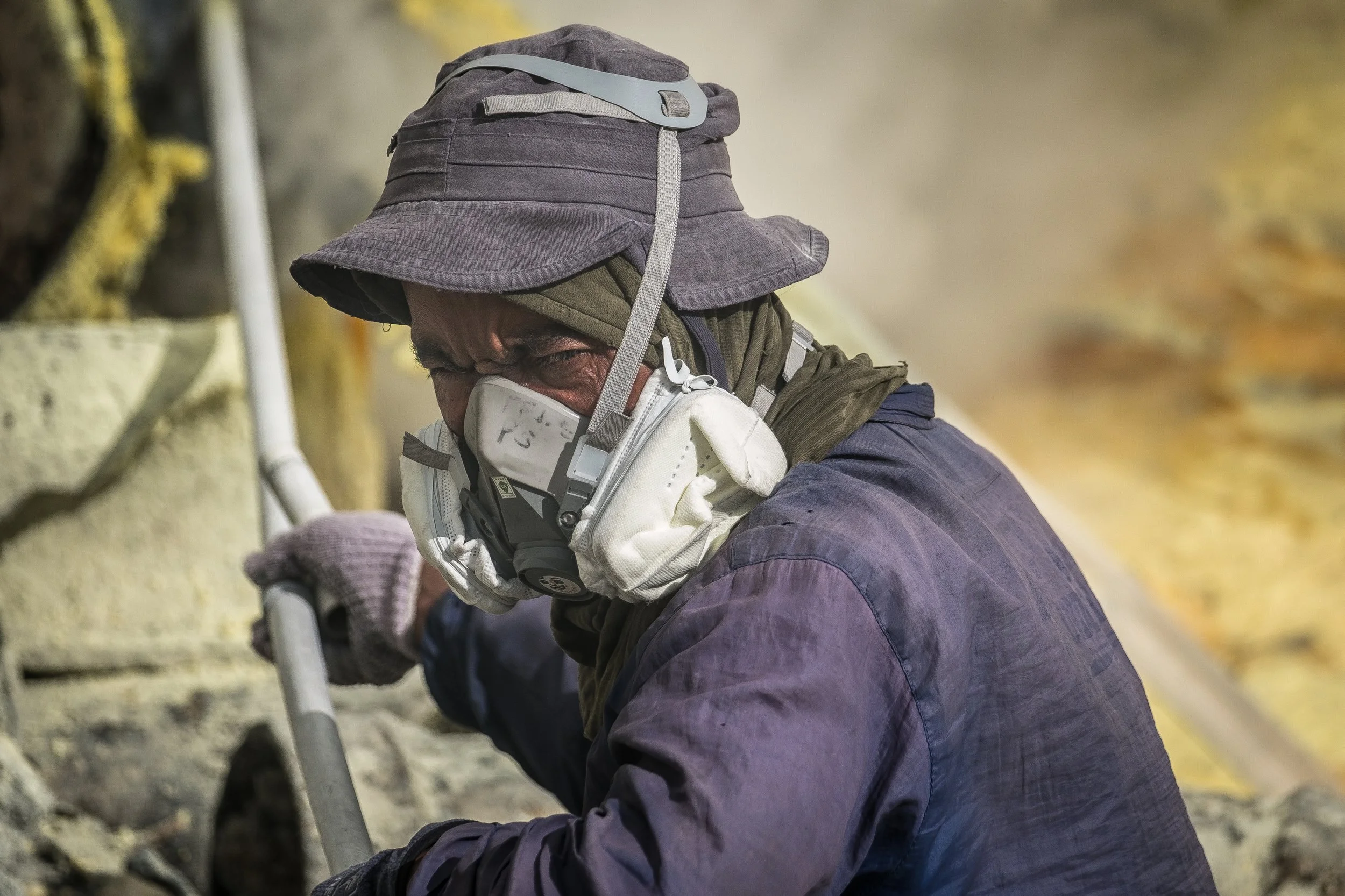Travailleur portant un bob et un masque de protection pour extraire du soufre.