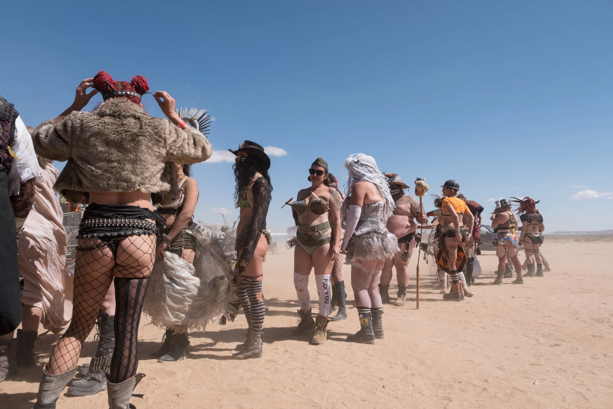 Groupe de personnes déguisées dans un désert pour un événement ou un festival, portant des costumes variés, certains avec des accessoires de fête ou de cosplay.