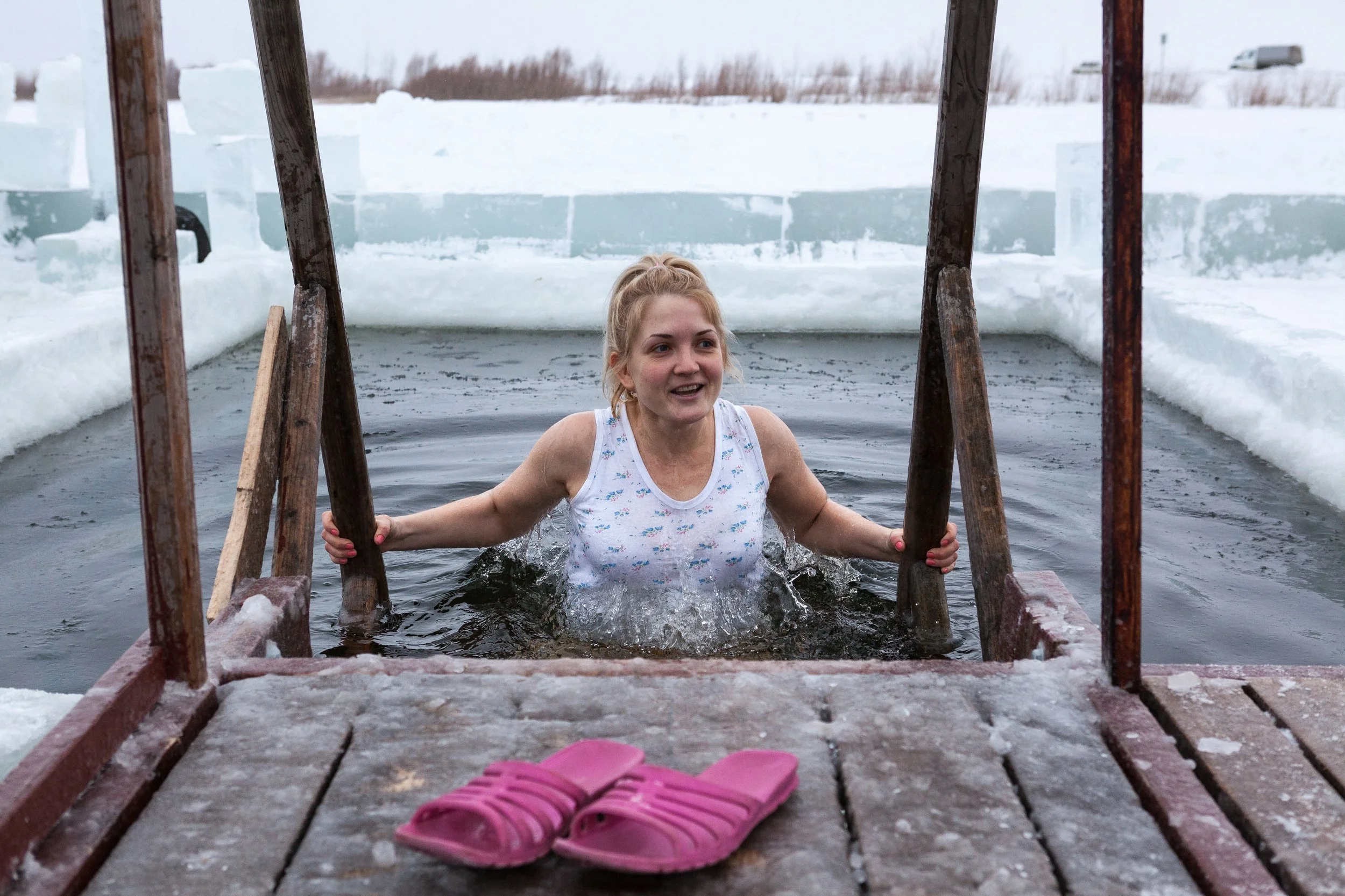 Femme sortant d'un bain glacé dans un lac gelé, avec des tongs roses sur le pont en bois, entouré de glace et de neige en Russie.