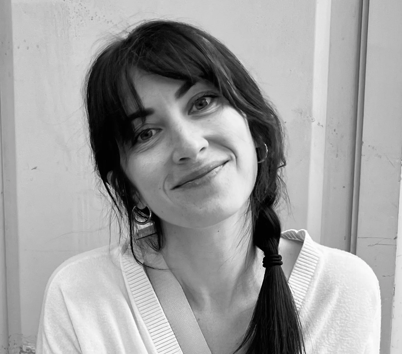 Black and white photo of a woman with dark hair in a braid, wearing a light sweater, smiling softly.