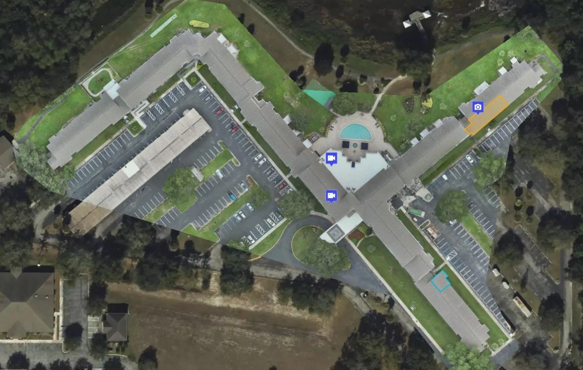 Aerial view of a large apartment complex with parking lots, a swimming pool, and surrounding greenery.