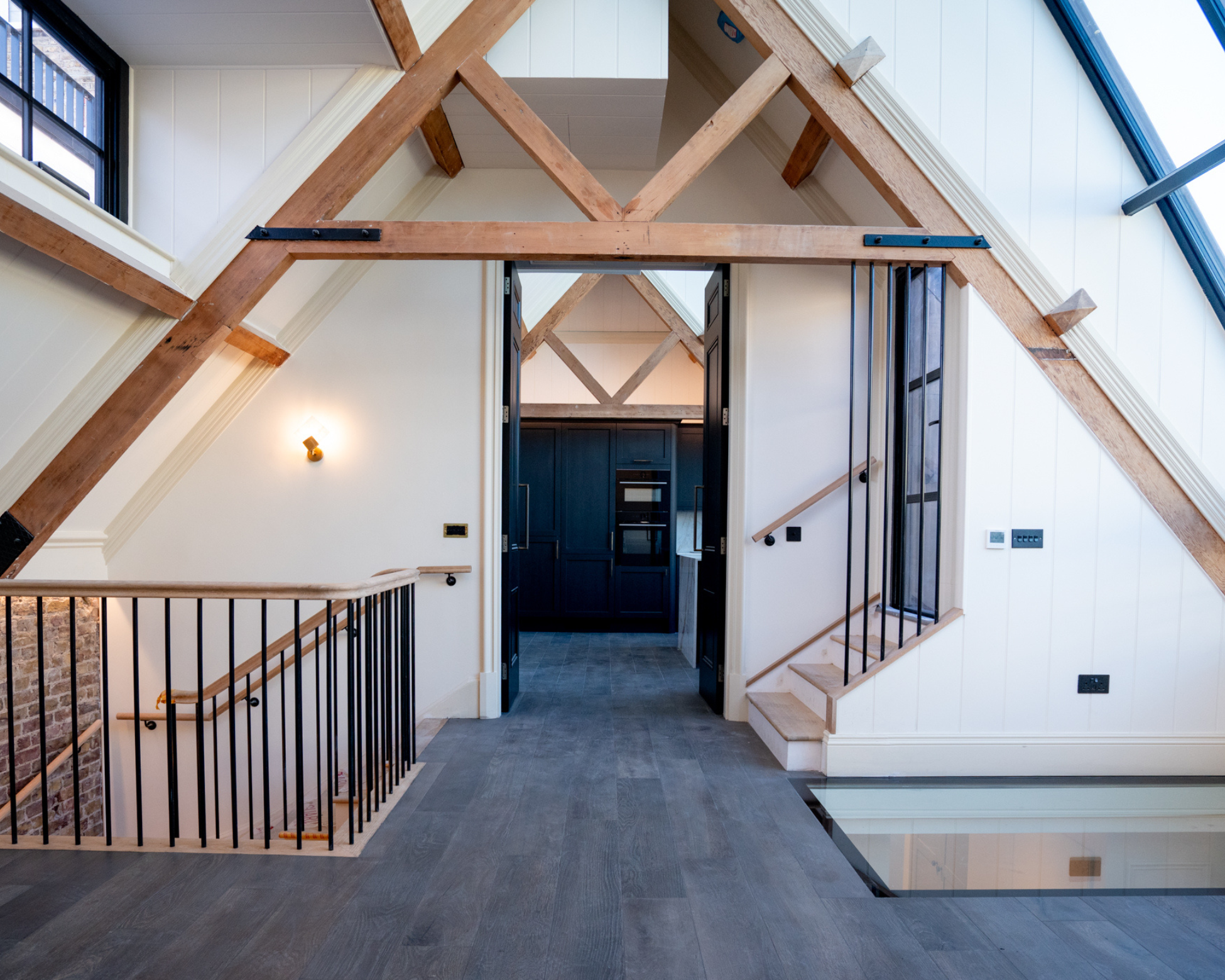 J&Co Architects Ltd — Interior mezzanine level of the Old Pottery Clapham conversion showing exposed oak roof trusses, steel balustrade and glass floor panel