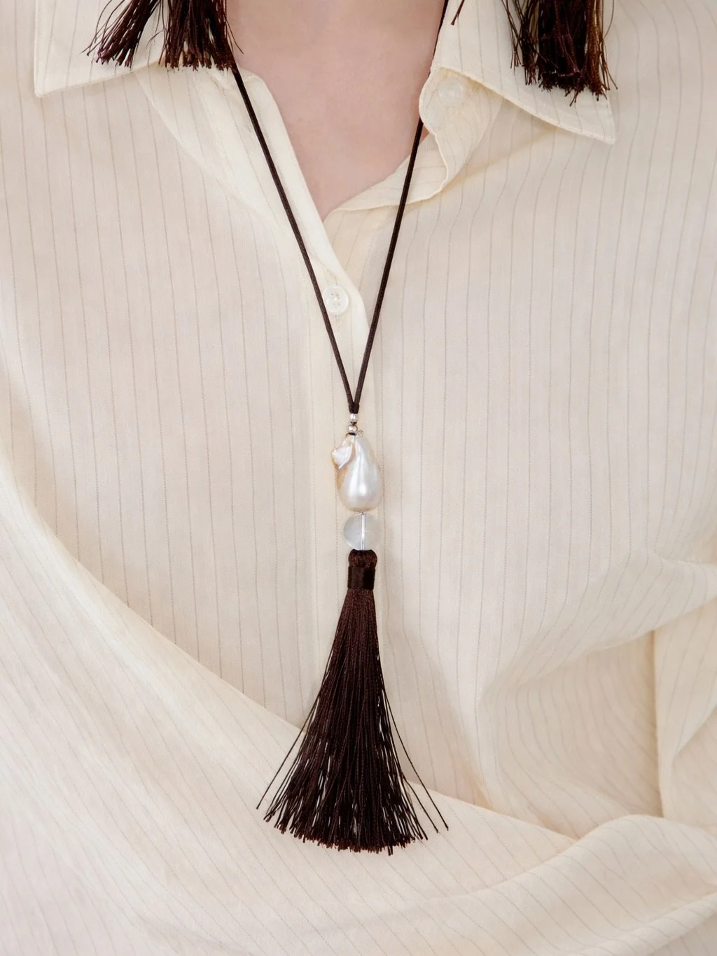 New in our CASCADE Pearl necklace. 

A keshi pearl and clear glass stone are suspended from a brown silk thread and finished with a flowing brown nylon tassel and silver details.