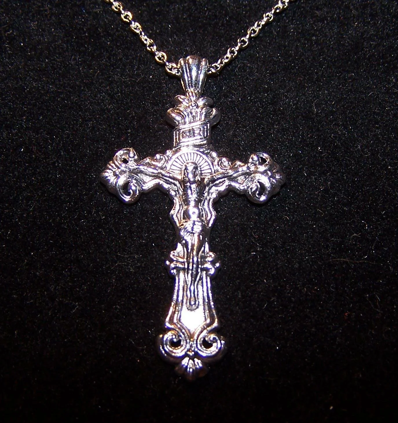 An image of a silver cross with some swirls on the cross ends and a Jesus crucified.