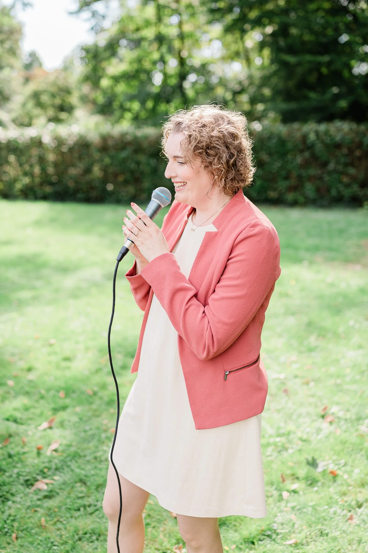 Traurednerin steht vor der Hochzeitsgesellschaft und hält ein Mikrofon in der Hand