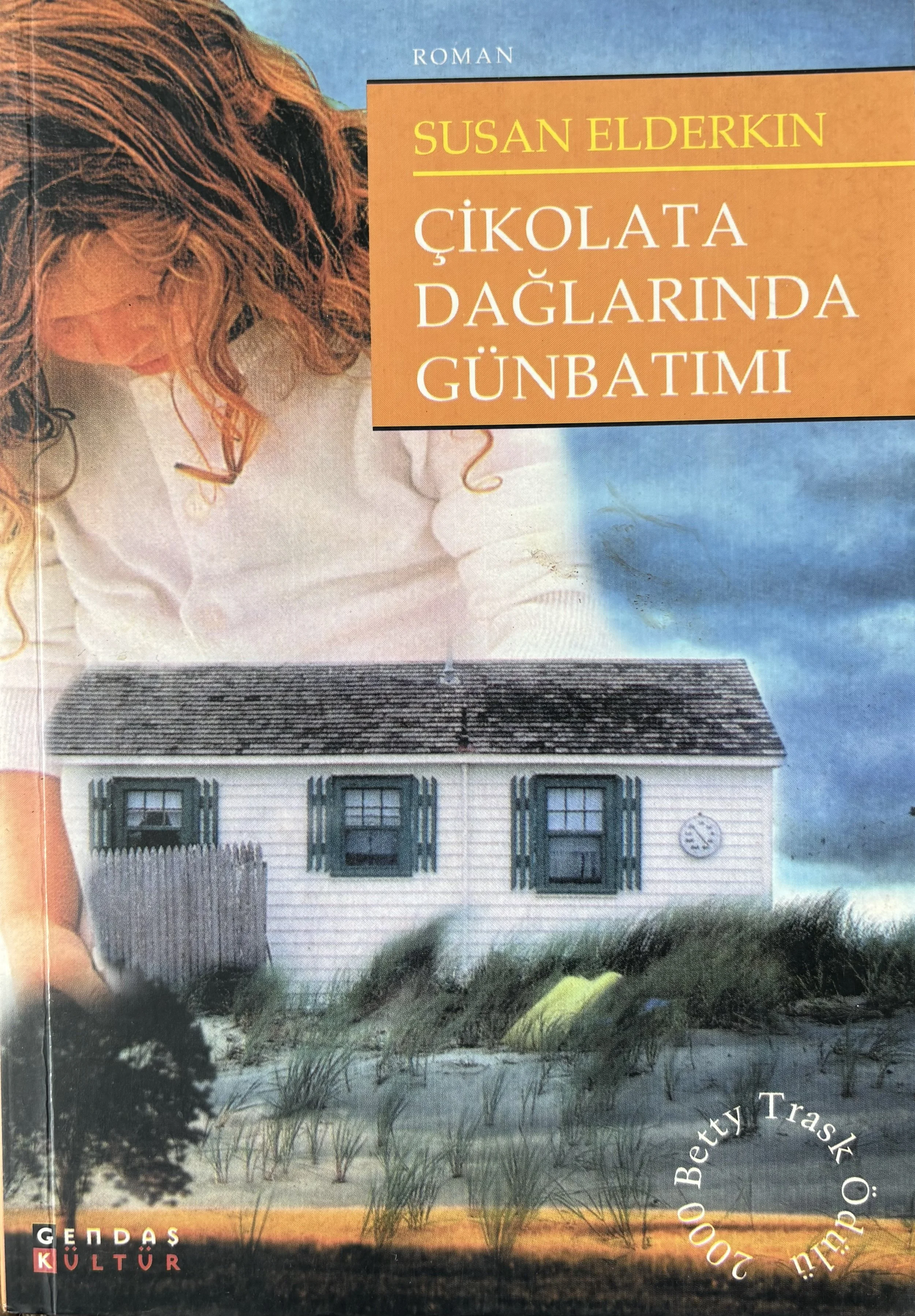 Book cover with a girl with curly red hair, a small house with green window shutters, and a cloudy sky, titled 'Chocolate Mountain Sunrise' by Susan Elderkin, published by Gendaş Kültür.