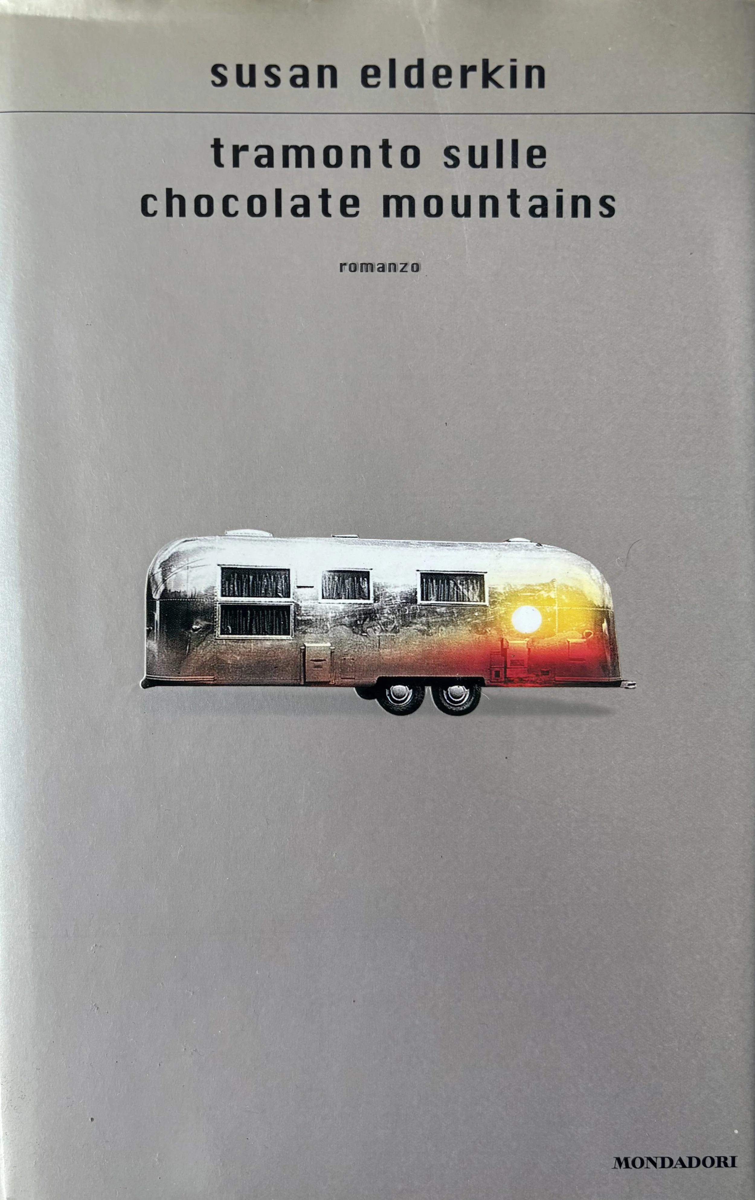 Book cover with the title 'Tramonto sulle chocolate mountains' by Susan Elderkin, featuring an image of a vintage silver camper trailer with a sunset reflected on it.