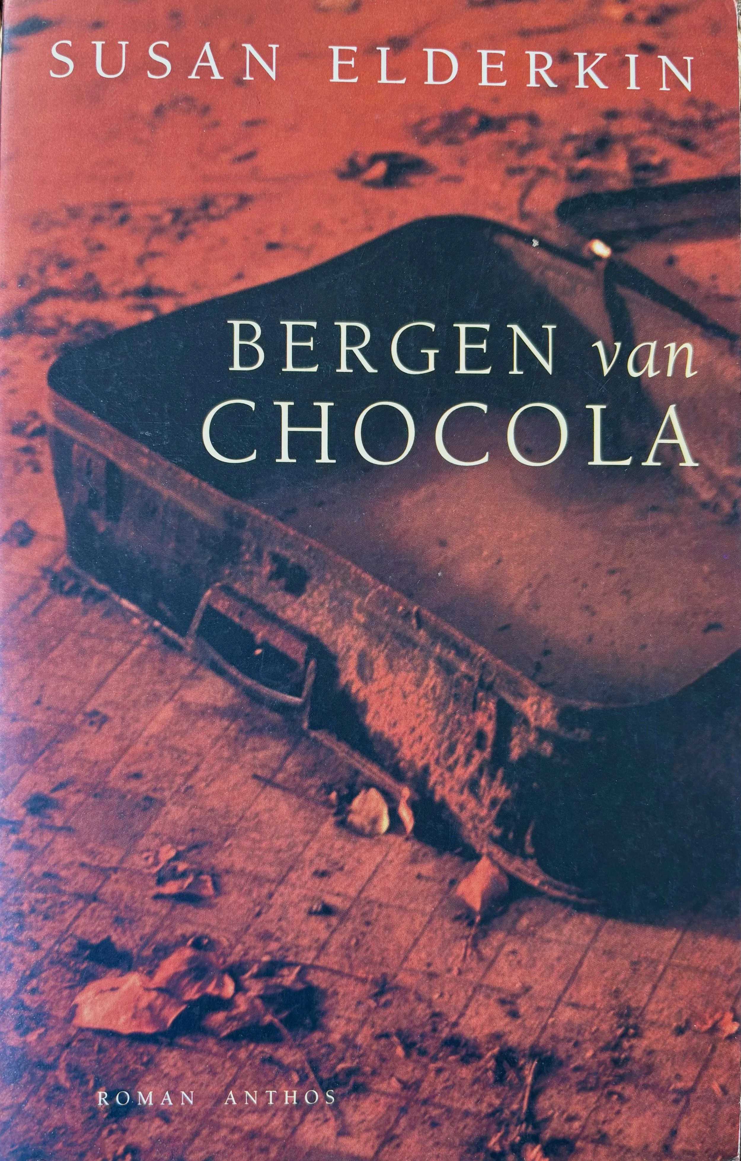 The cover of a book titled 'Bergen van Chocola' by Susan Elderkin, featuring a photograph of an old, empty, rusty suitcase on a weathered wooden floor with scattered leaves, depicted in reddish tones.