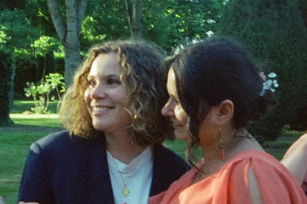 Un couple de femmes souriantes en conversation dans un parc verdoyant, entourées d'arbres, lors d'une journée ensoleillée.