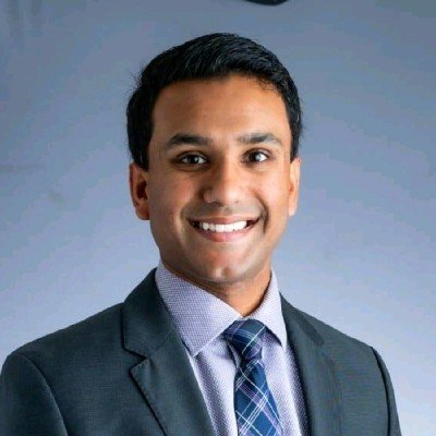 Professional man in a suit smiling at the camera with a light blue background.