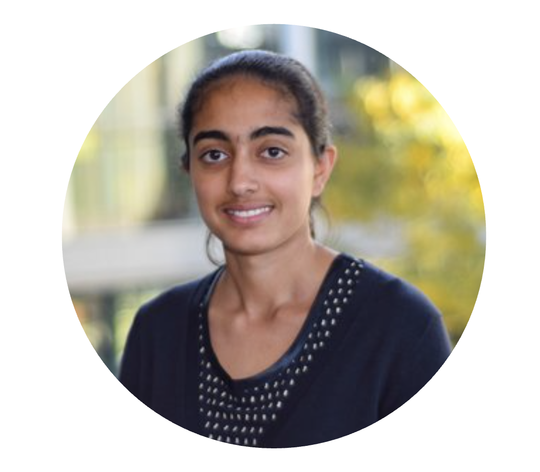 Portrait of a young woman with dark hair tied back, smiling, outdoors with blurred greenery background.