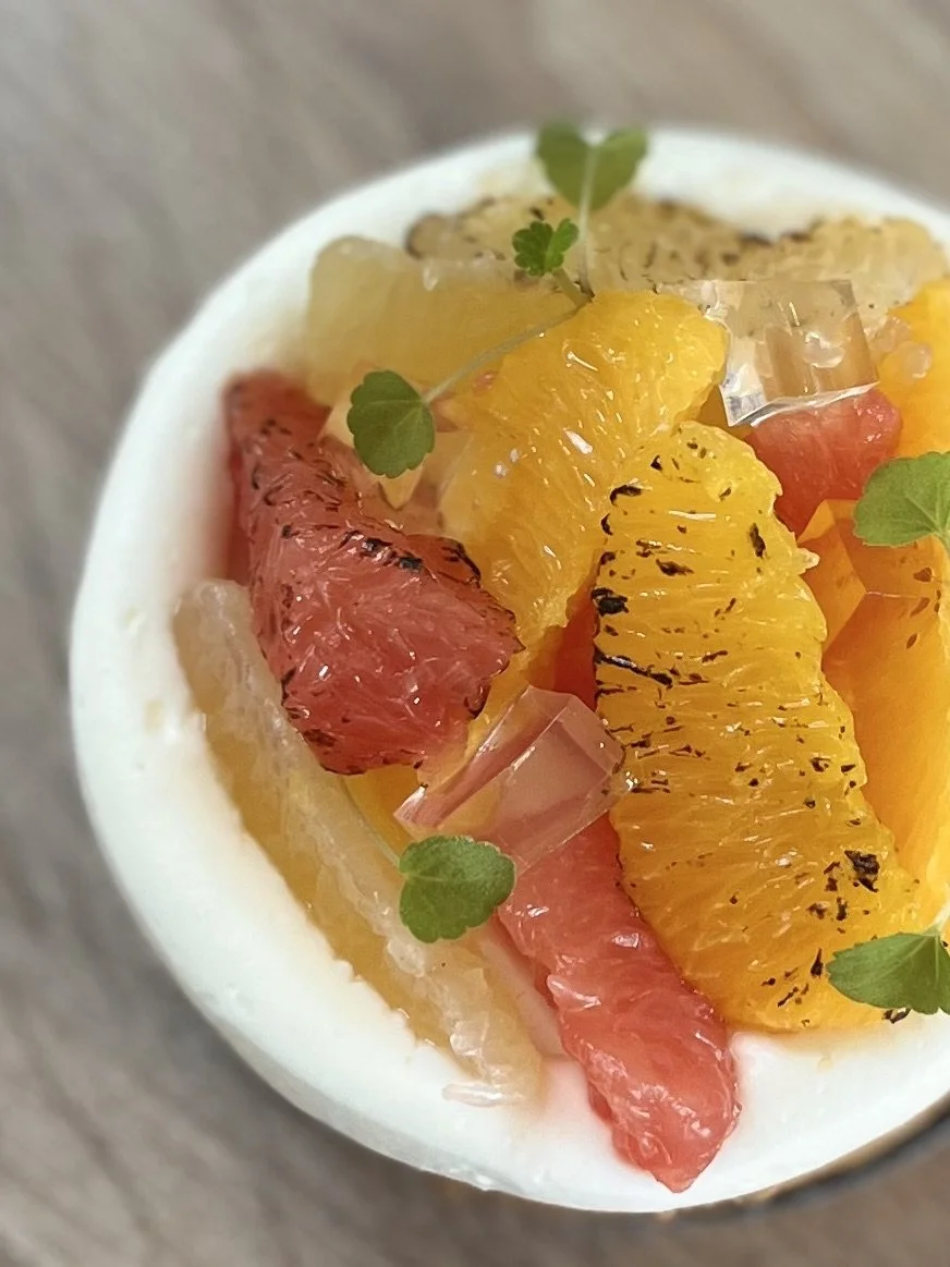 Dessert avec des morceaux d'agrumes comme pamplemousse, orange et cédrat, décoré de petites feuilles vertes.