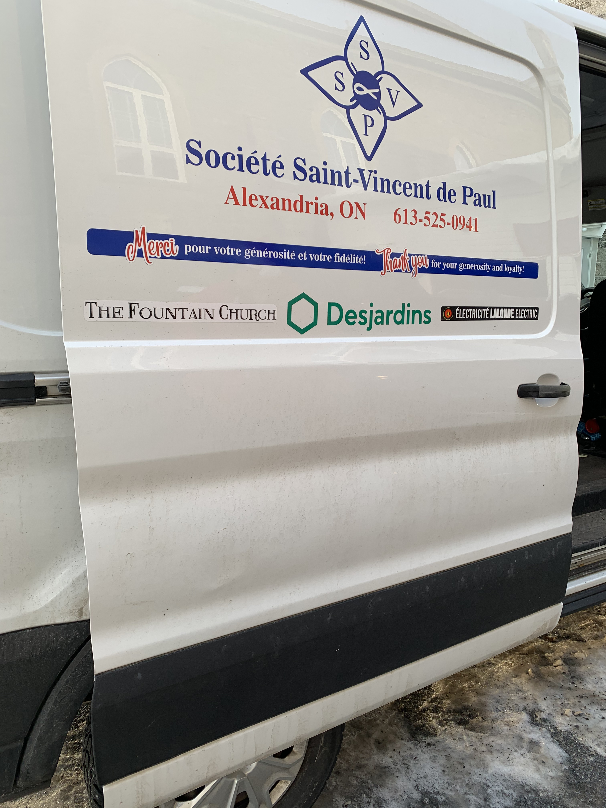 Sign on a white vehicle for Société Saint-Vincent de Paul in Alexandria, Ontario, with logos of The Fountain Church, Desjardins, and Électricité Lalonde Electric, and text thanking for generosity and loyalty.