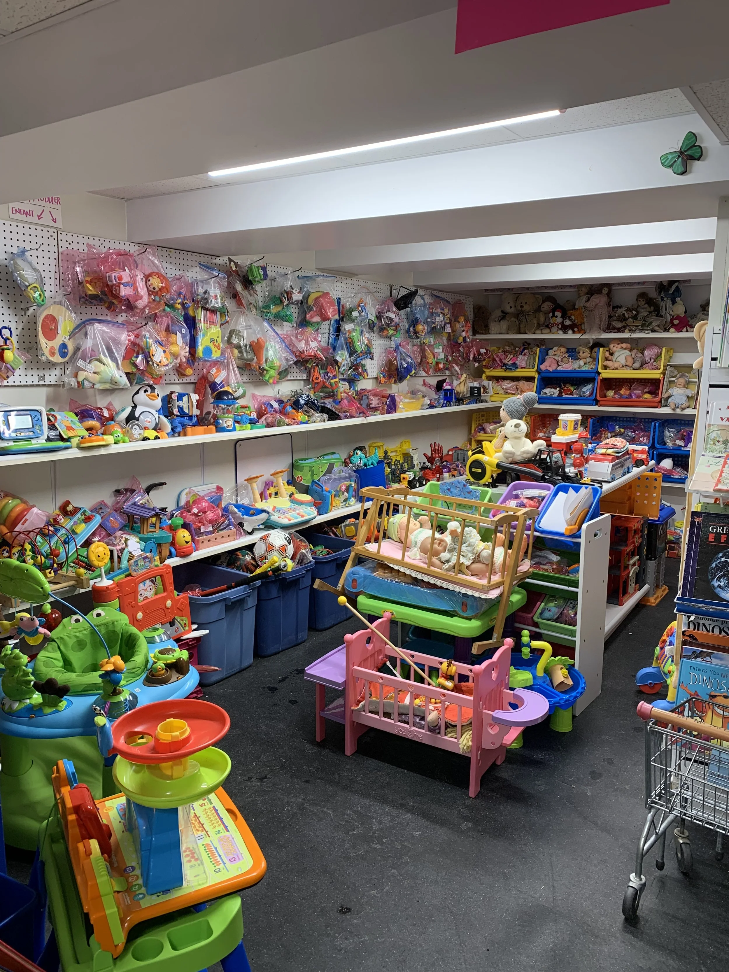 A toy store aisle filled with various toys, including dolls, plush animals, and plastic playsets, organized on shelves and in bins.