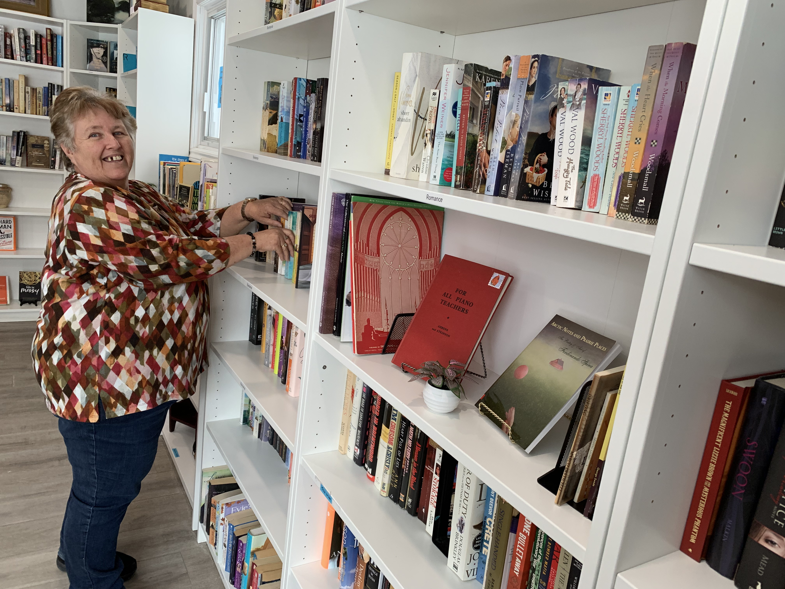 A woman shopping for books in a bookstore or library, smiling while browsing shelves filled with a variety of books.