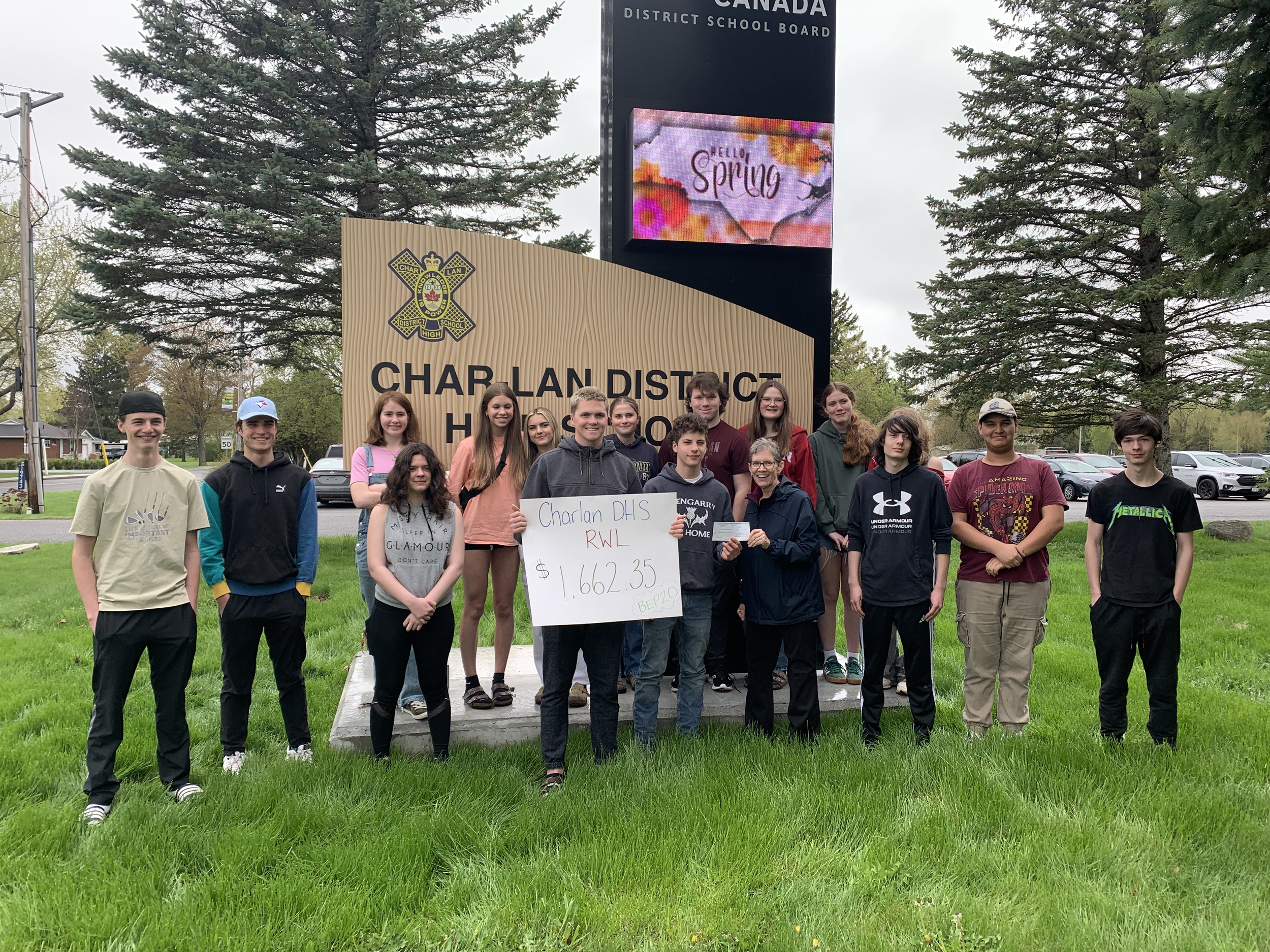 Group of students and teachers standing in front of Char-Lan District High School sign, holding a large check for $1,662.35 for the RWL charity, with trees and parked cars in the background.