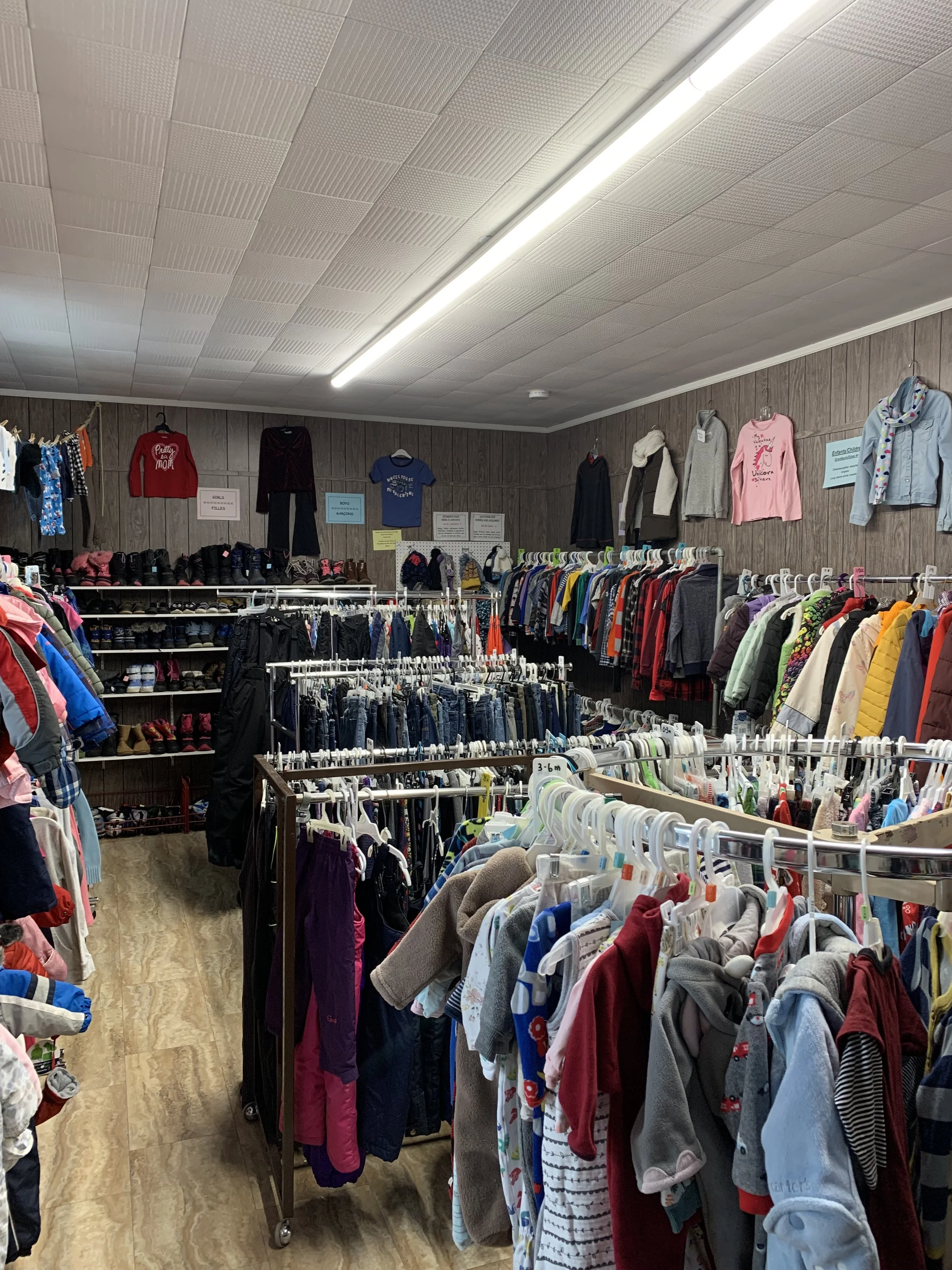 Interior of a thrift store with racks of children's clothing and shoes on shelves in the background.