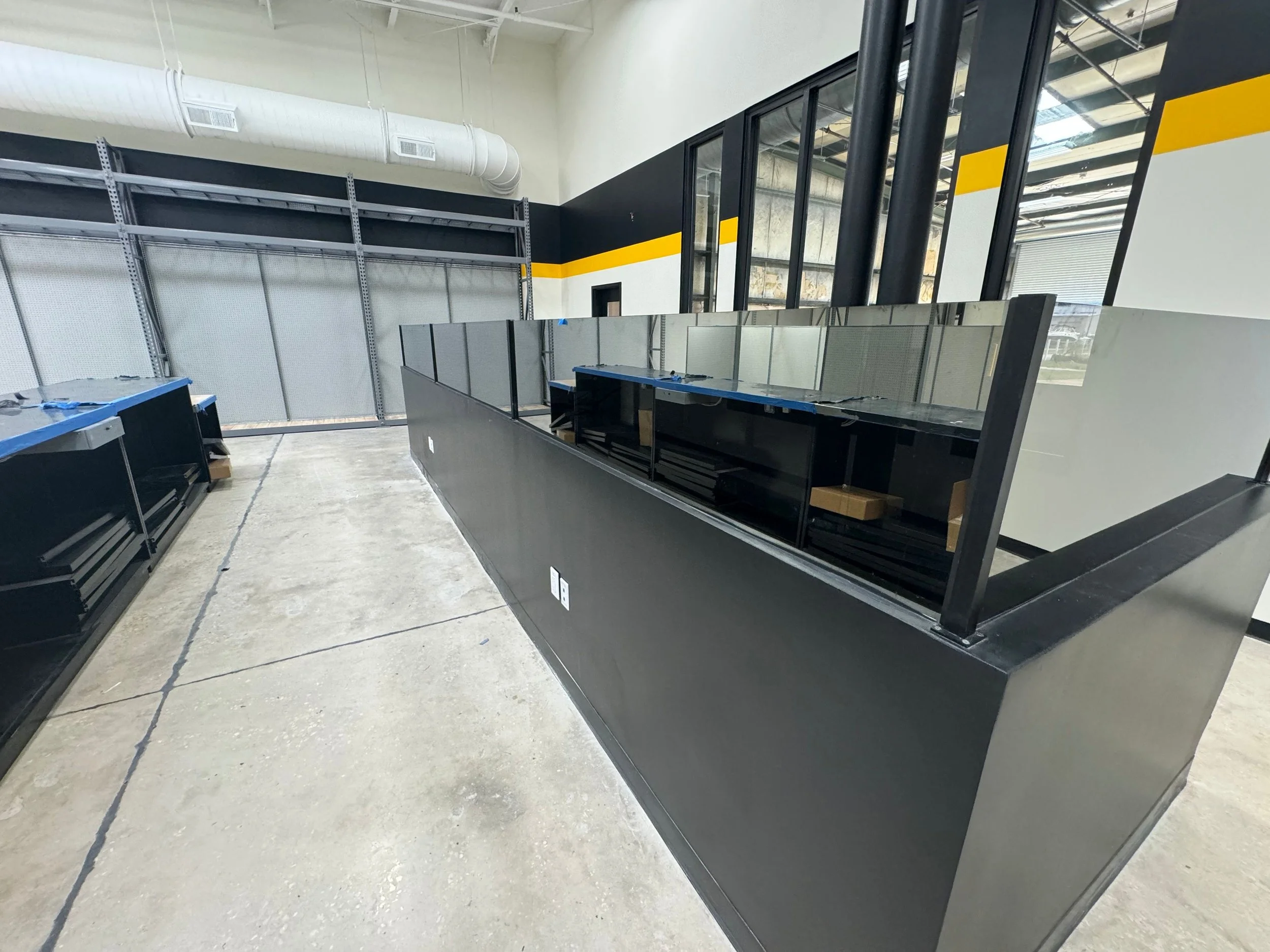 Empty retail or commercial store space with black retail counters, large windows, and industrial ceiling with ductwork.