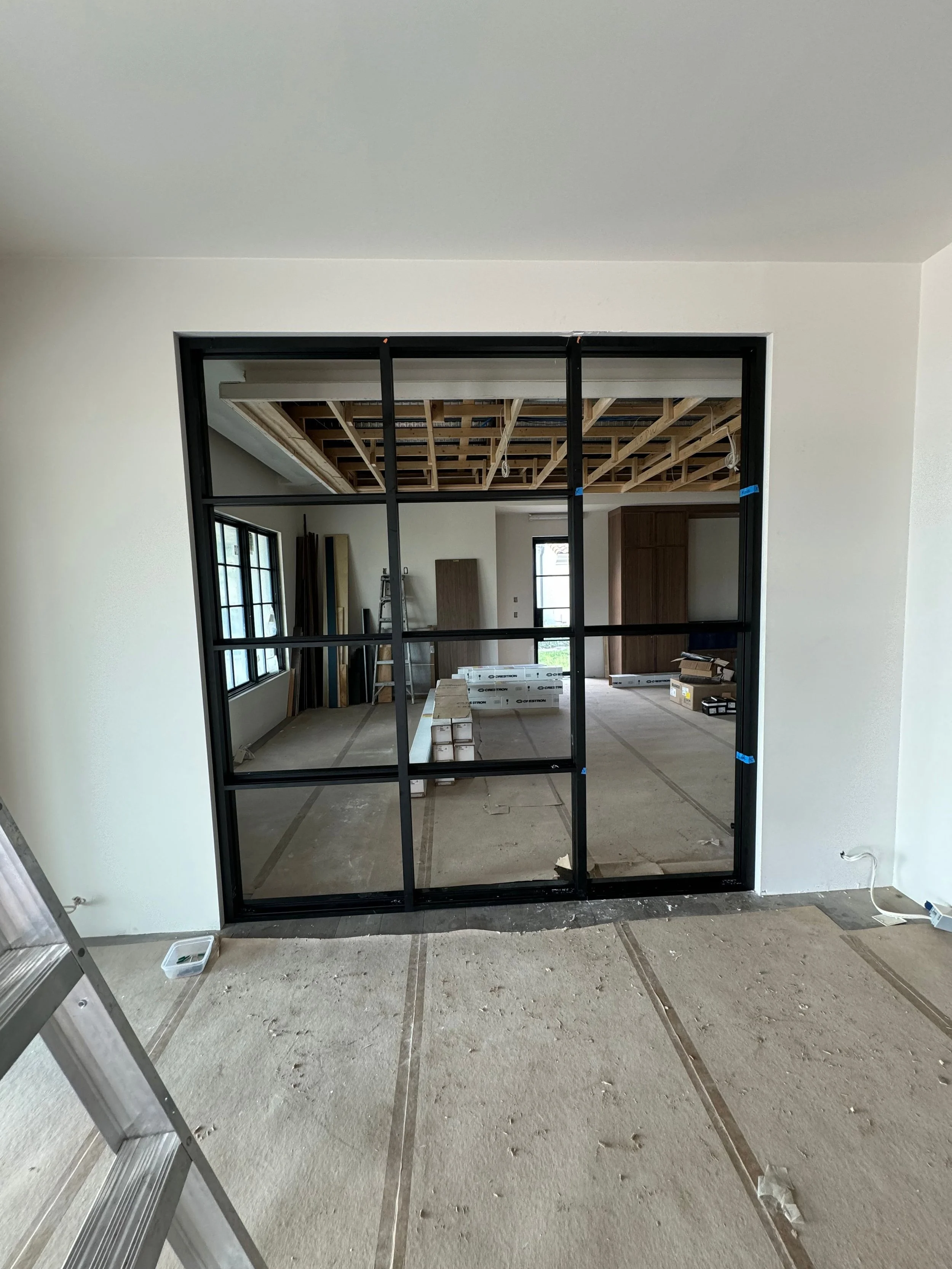 Interior of a room under construction with a black metal framing for a partition or wall, construction materials, and tools visible in the background.