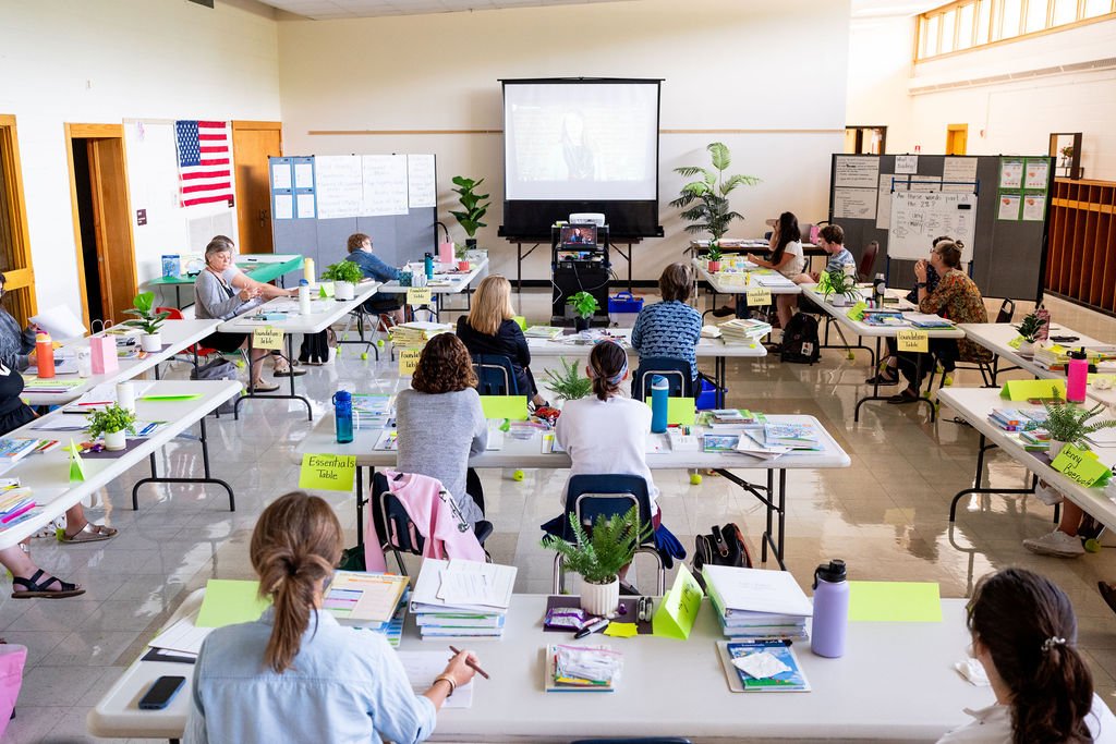 Smiling school children sitting in classroom, boy with brown hair in dark blue jacket and girl with braids in white shirt.