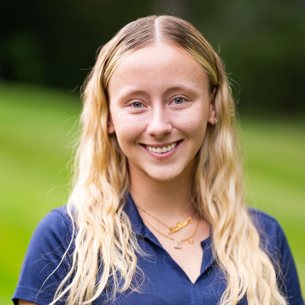 A young blonde woman, smiling, blue shirt, outdoors