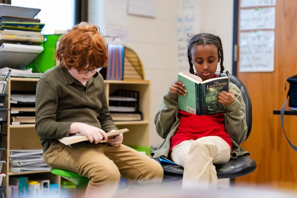 Two Feller School students reading books in armchairs