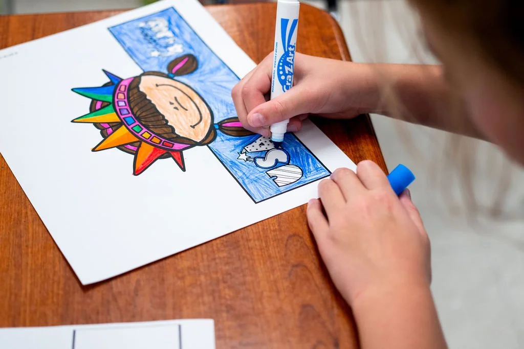 Child coloring a patriotic unicorn on a piece of paper with colored markers.