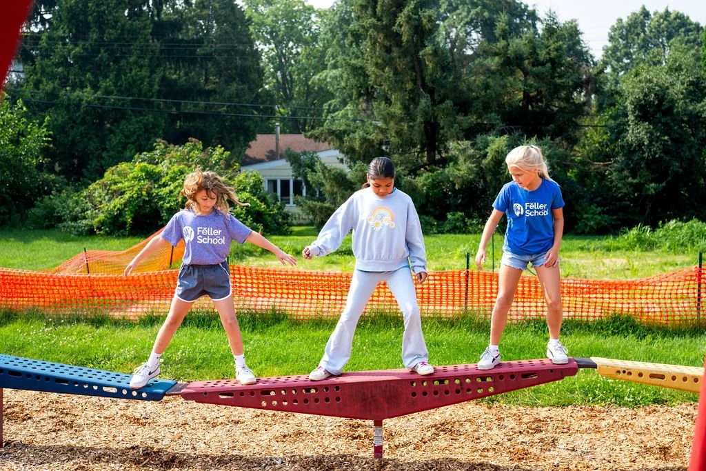 Three girls balancing on a red seesaw in a park.