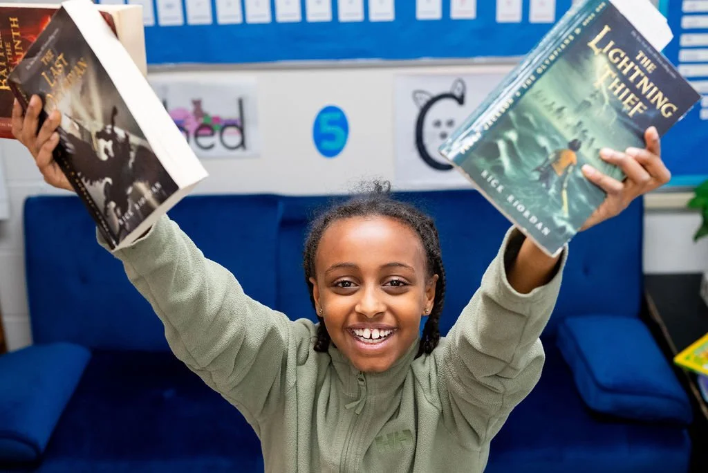 A Feller School student holding a chapter book above her head