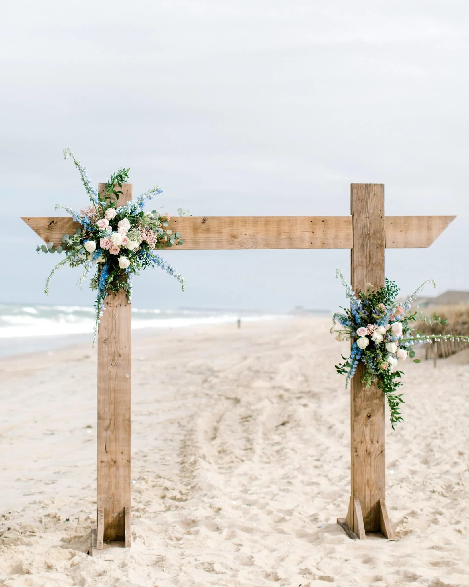 Wooden wedding arch decorated with pink and white flowers on a beach.