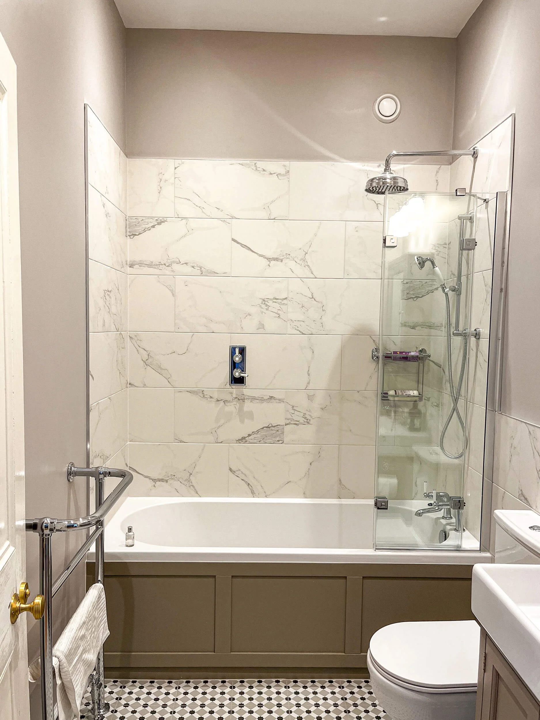Bathroom with bathtub, marble tile wall, glass shower enclosure, toilet, and a towel rack.