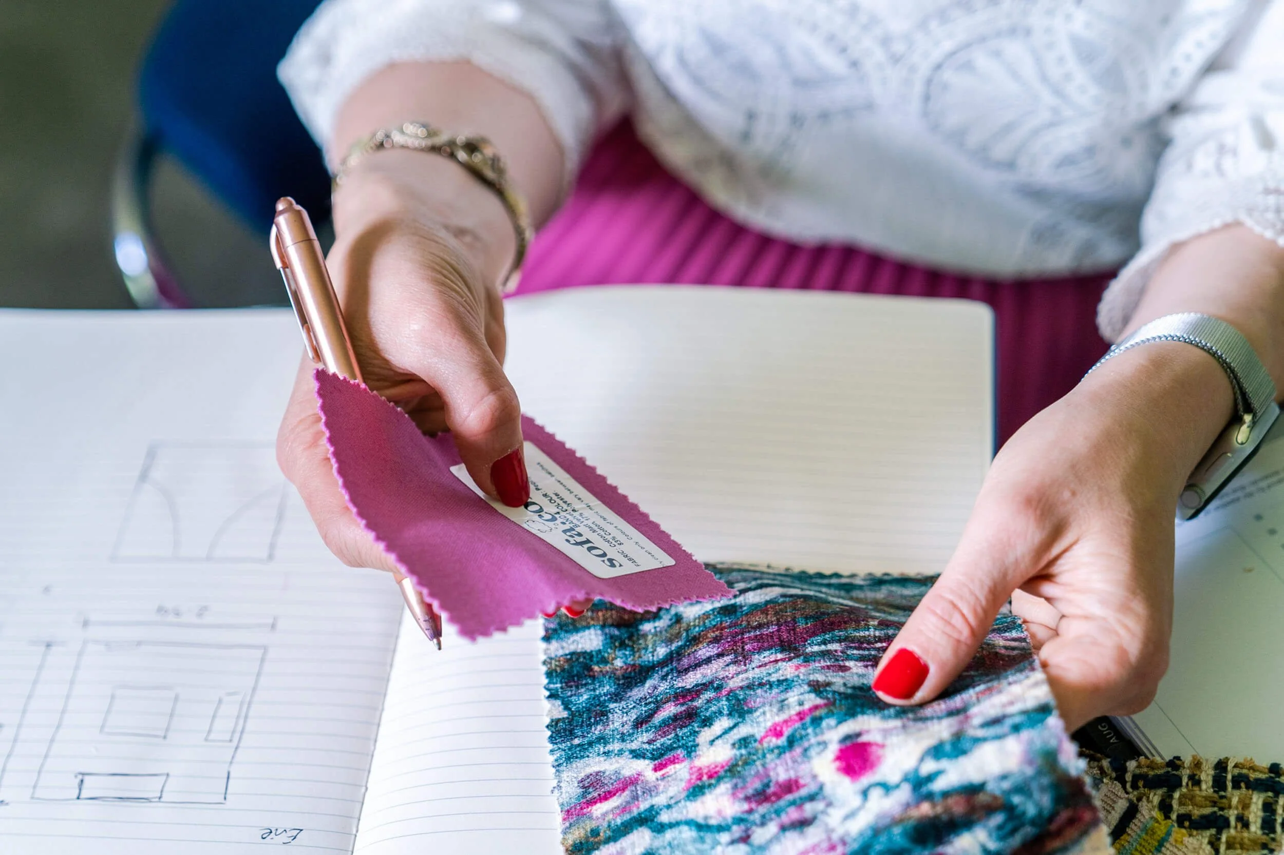 Person holding a fabric swatch and a color card, taking notes in a notebook.