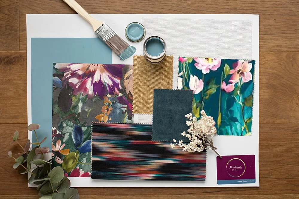 Interior design mood board with fabric swatches, paint samples, floral prints, and decorative elements on a white board.