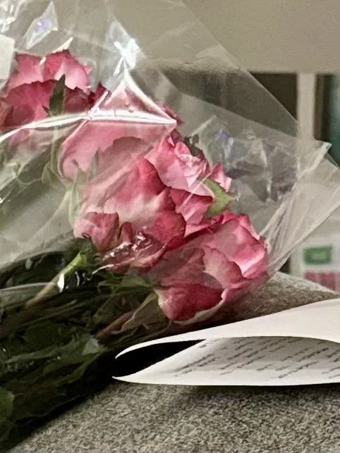 Bouquet of pink roses wrapped in plastic pictured alongside the folded handwritten letter; a portion of the note is visible.