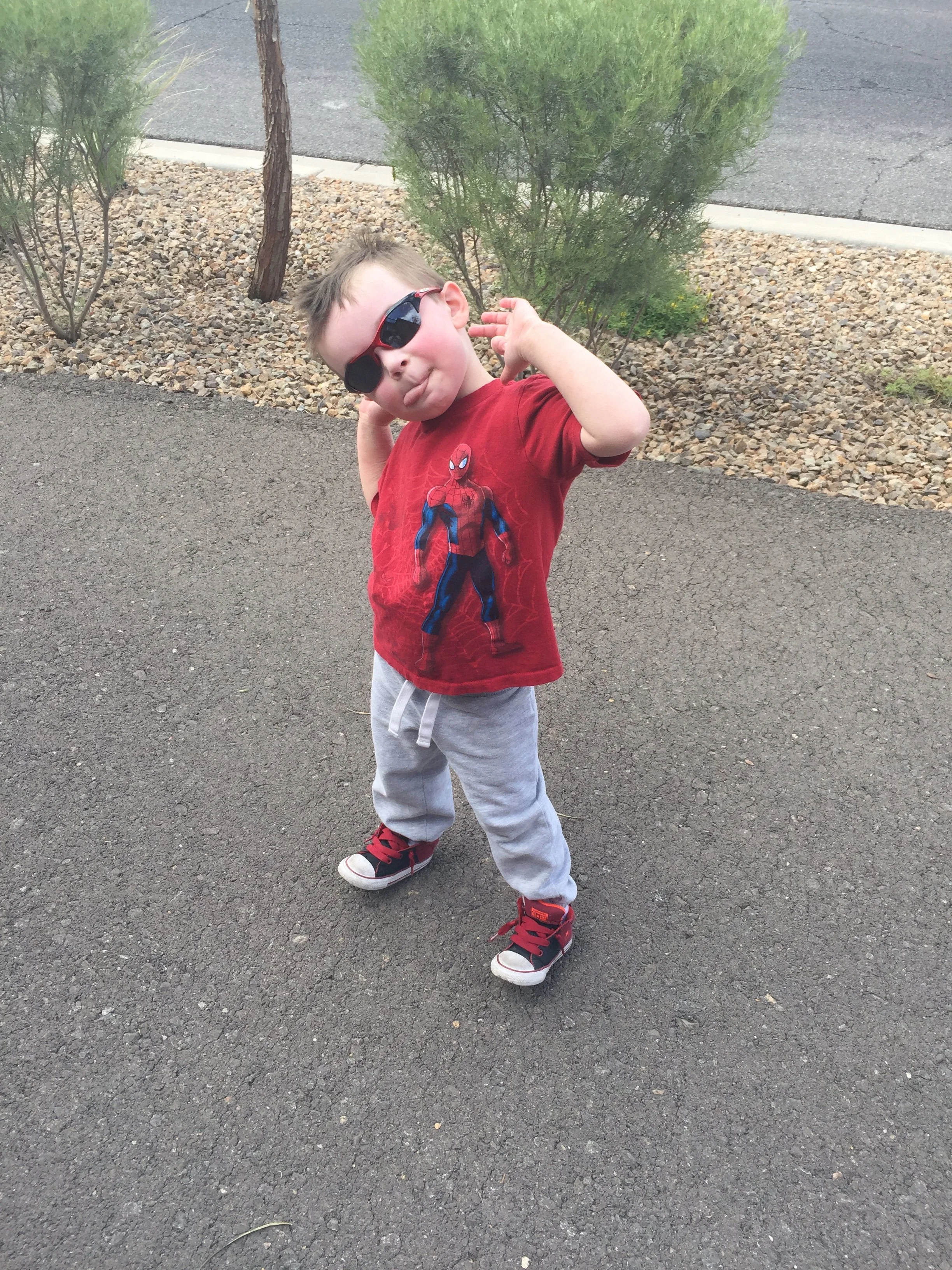 Young child wearing sunglasses and a red shirt posing on a paved walking path.