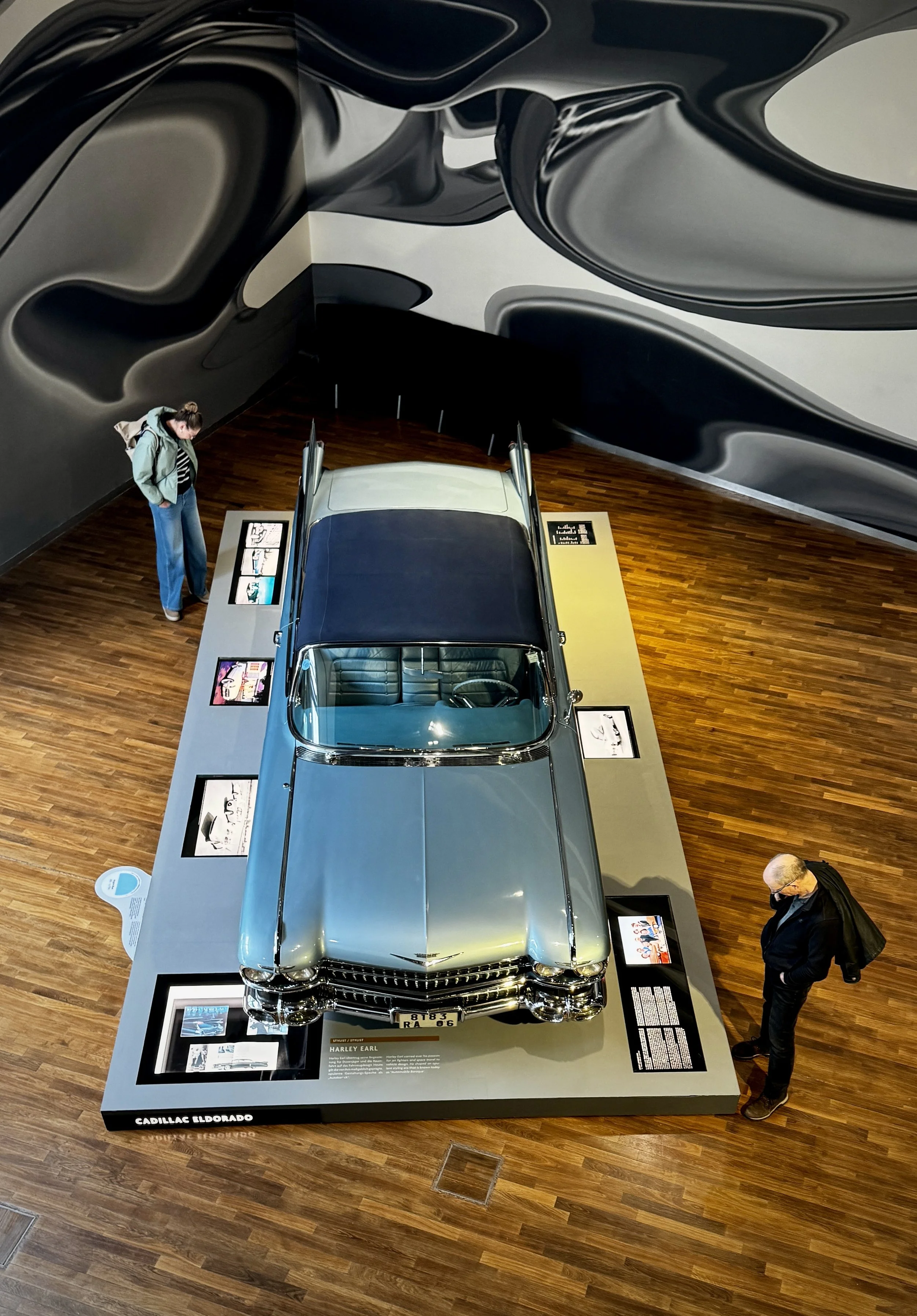 A top-down view of a classic Cadillac surrounded by exhibits and curved walls inside Autostadt in Wolfsburg, Germany.
