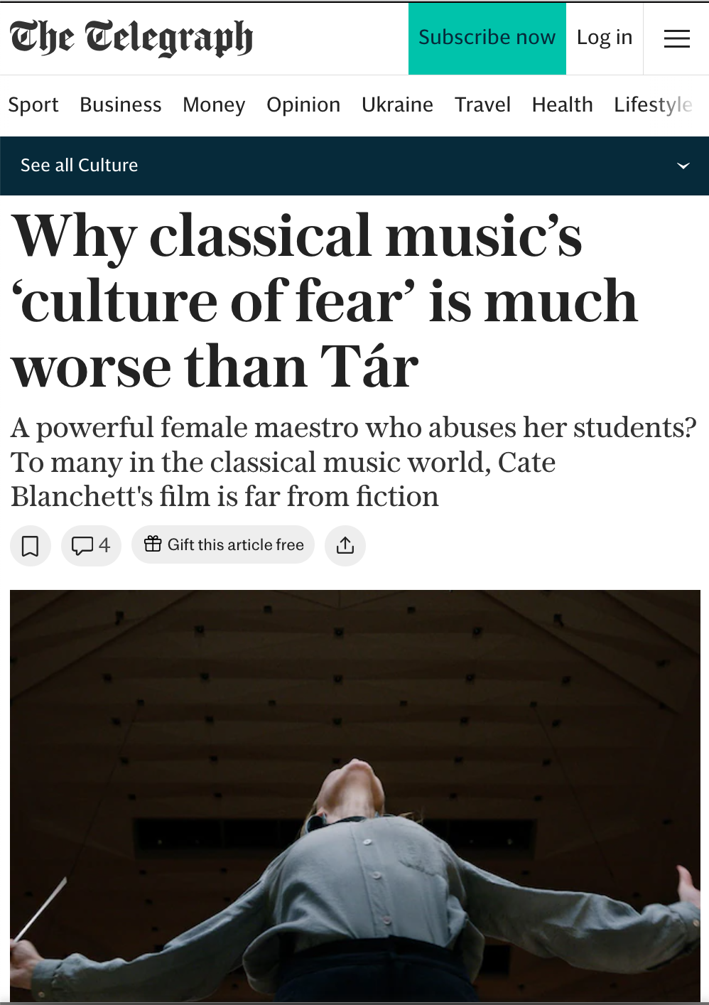 A person standing with their arms outstretched and head tilted back under a wooden ceiling, possibly conducting or performing in a large hall.