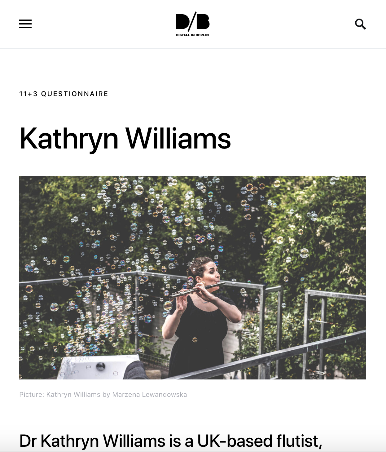 A woman playing the flute outdoors surrounded by floating bubbles, with green foliage in the background.