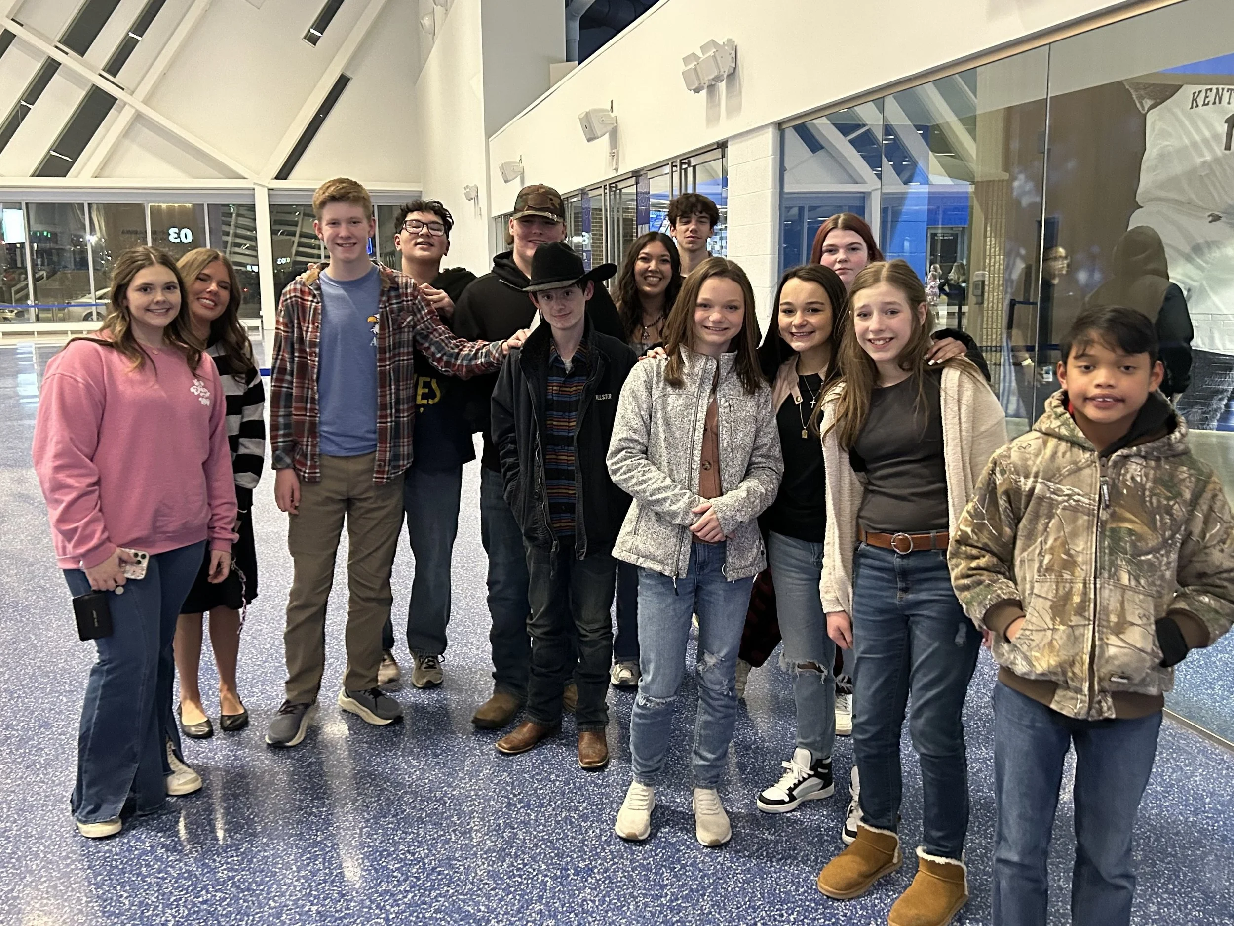 Group of teenagers in an airport terminal, smiling and posing for a photo.