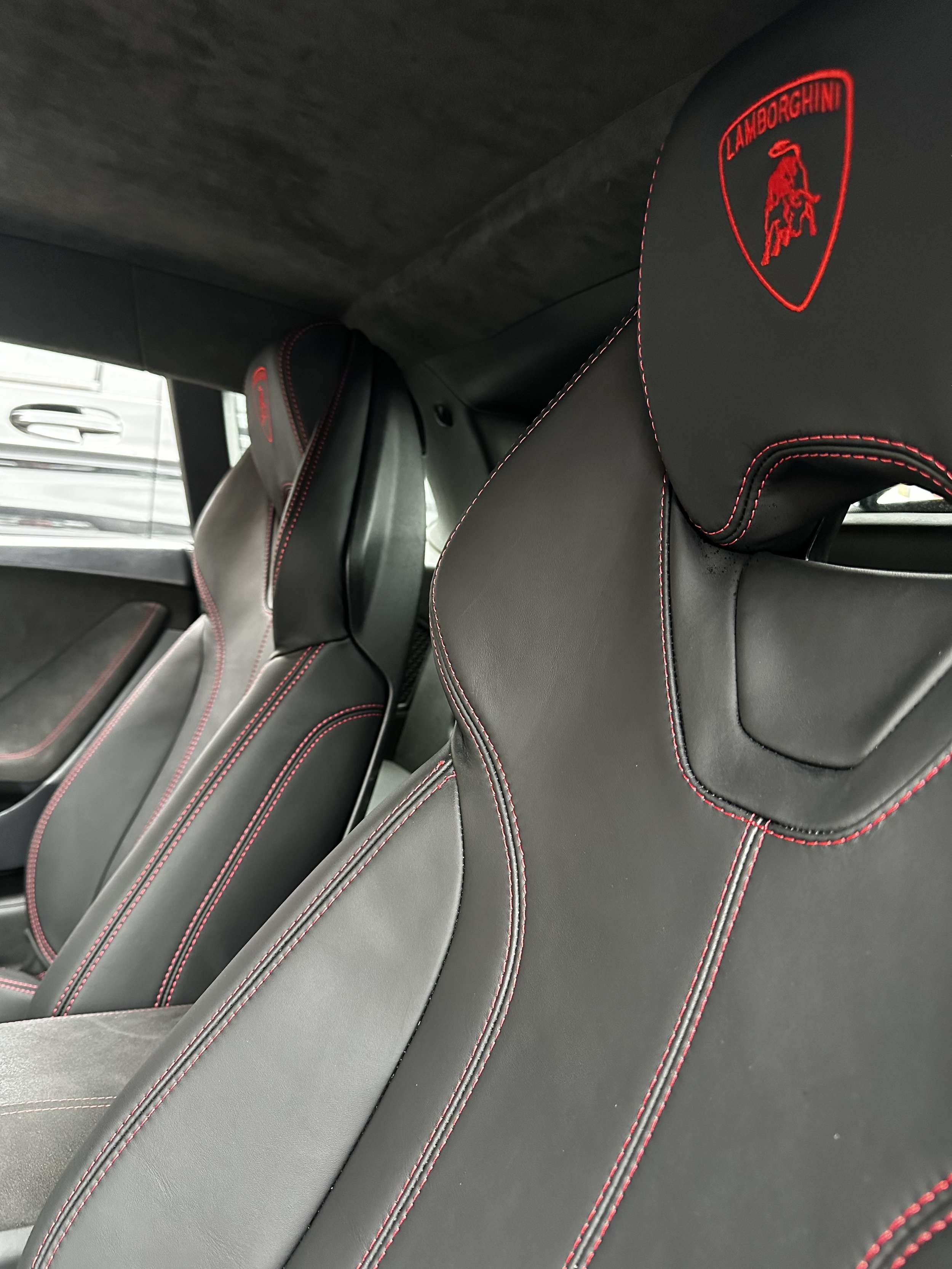Close-up of black leather car seats with red stitching and an embroidered Lamborghini logo on the headrest.