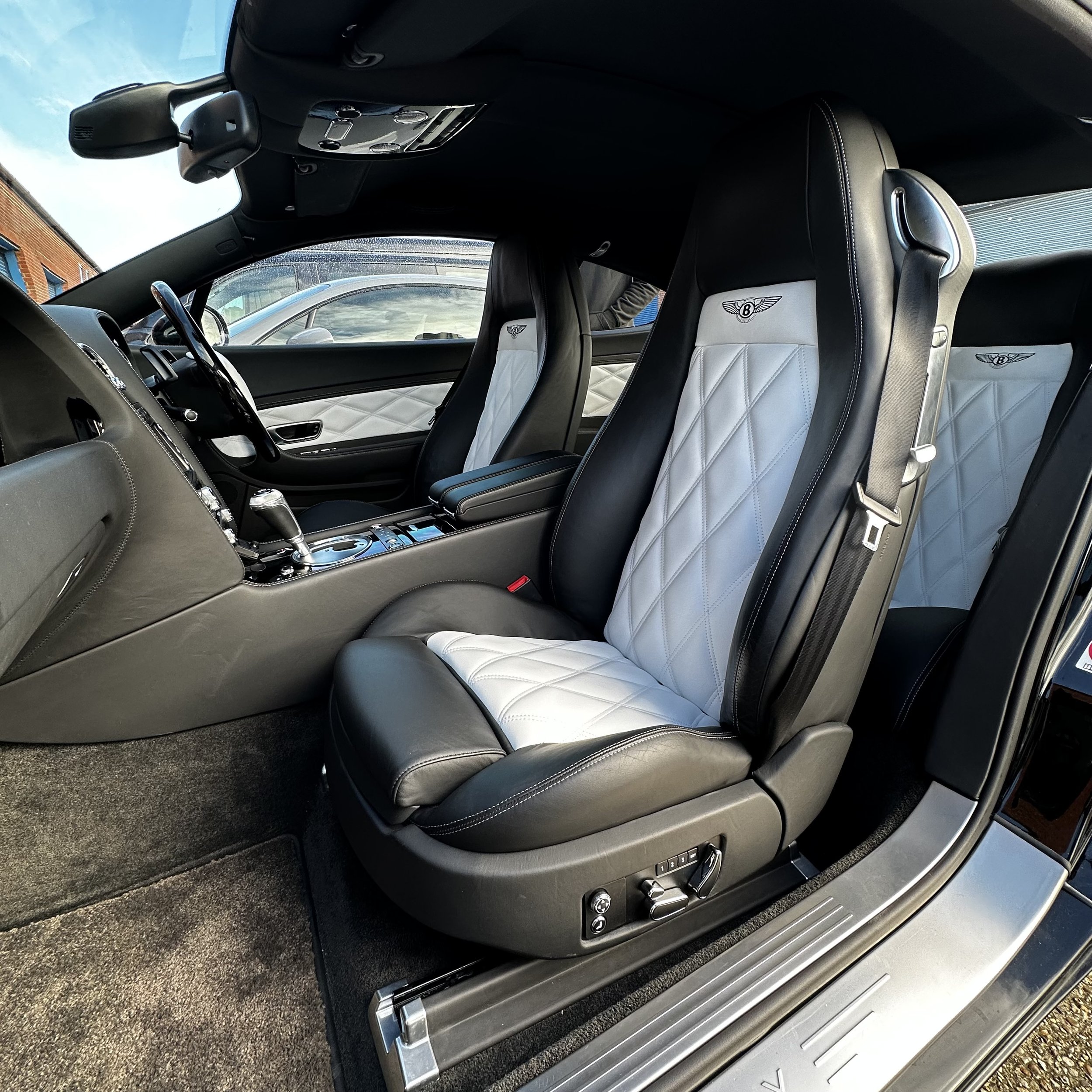 Inside the luxury car, featuring white quilted and black seats, a center console, and dashboard with controls and gear shifter.