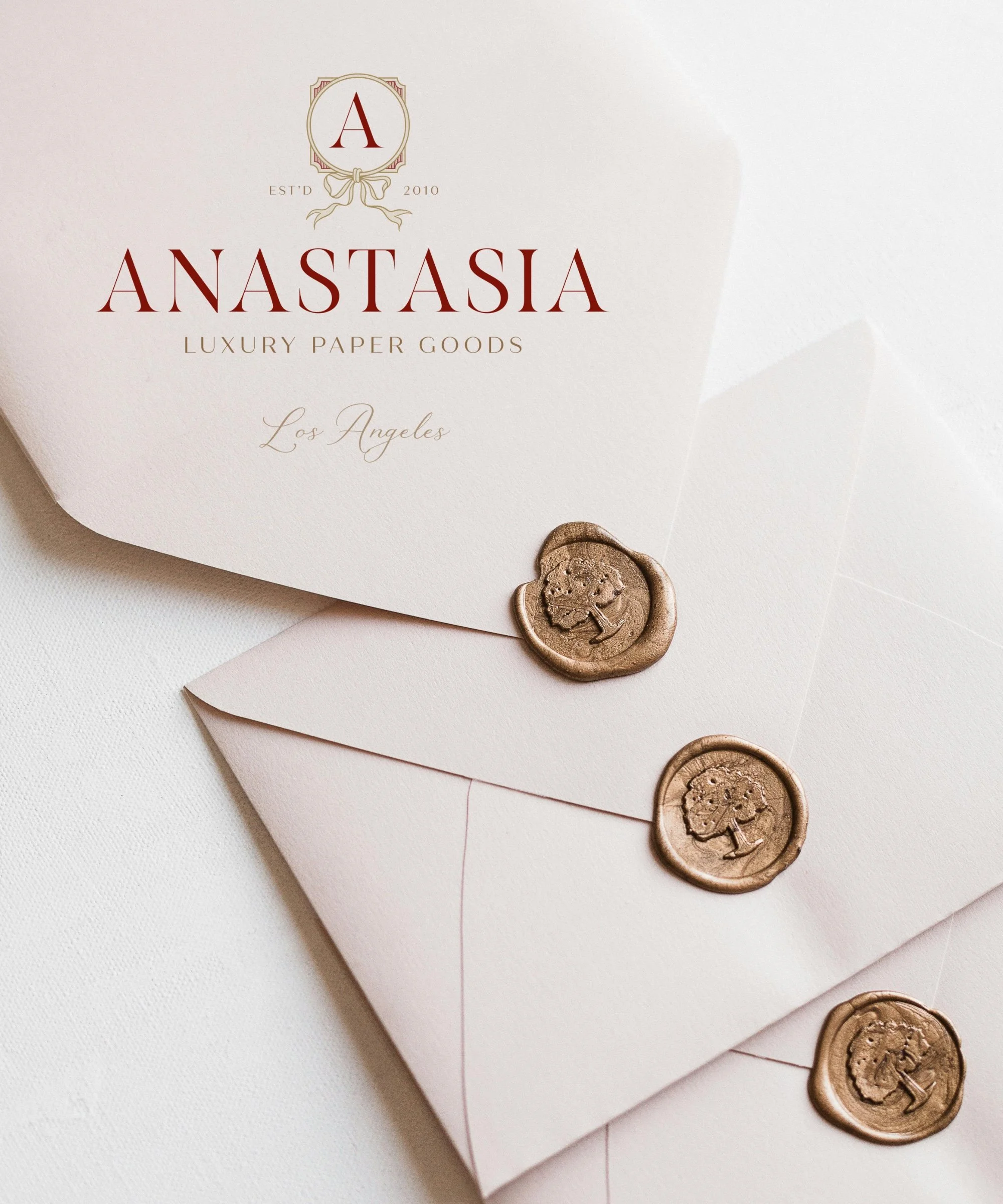 Three elegant pale pink envelopes sealed with gold wax stamps featuring a tree design. One envelope's card inside reads 'Anastasia Luxury Paper Goods Los Angeles' in stylish font.