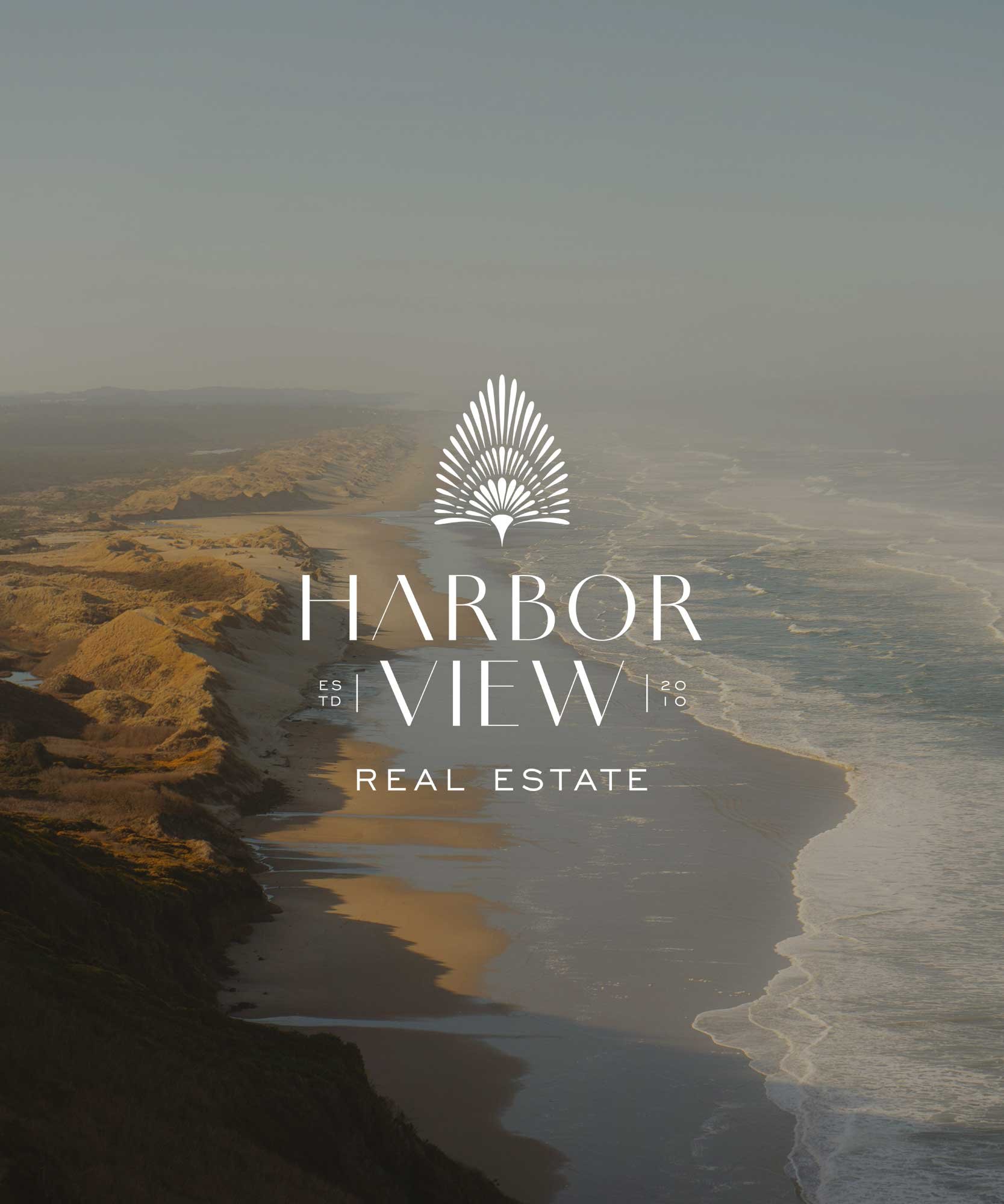 Aerial view of a coastline with cliffs and sandy beach, calm ocean waves, and a hazy sky, overlaid with text reading 'Harbor View Real Estate'.
