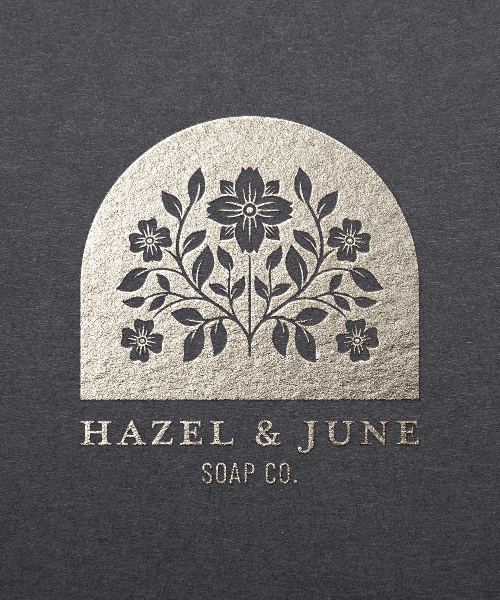 Black soap packaging with a silver floral logo and the text 'Hazel & June Soap Co.' underneath.
