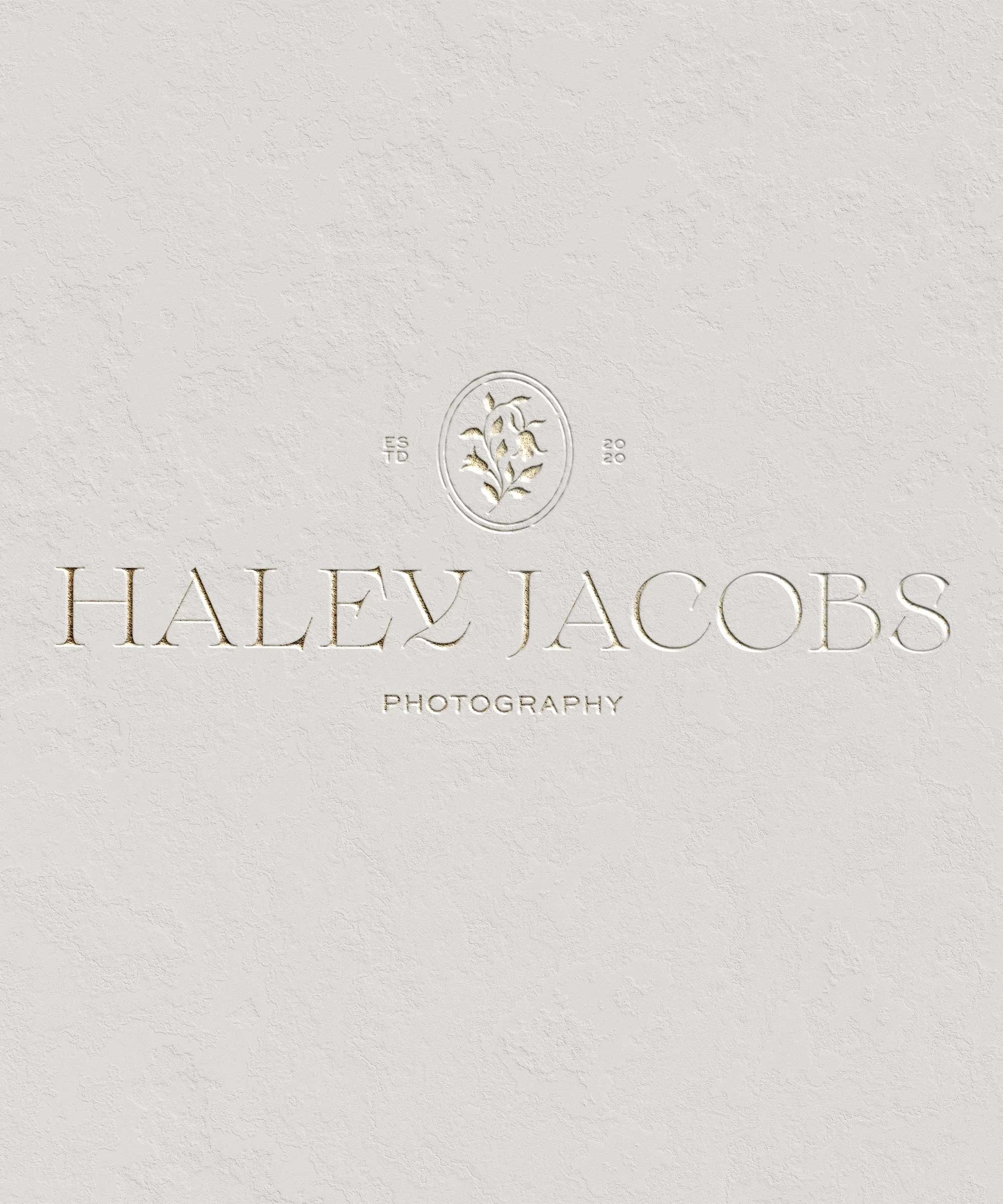 Elegant white textured background with embossed gold and silver text that reads 'Haley Jacobs Photography' accompanied by a logo of a floral design.