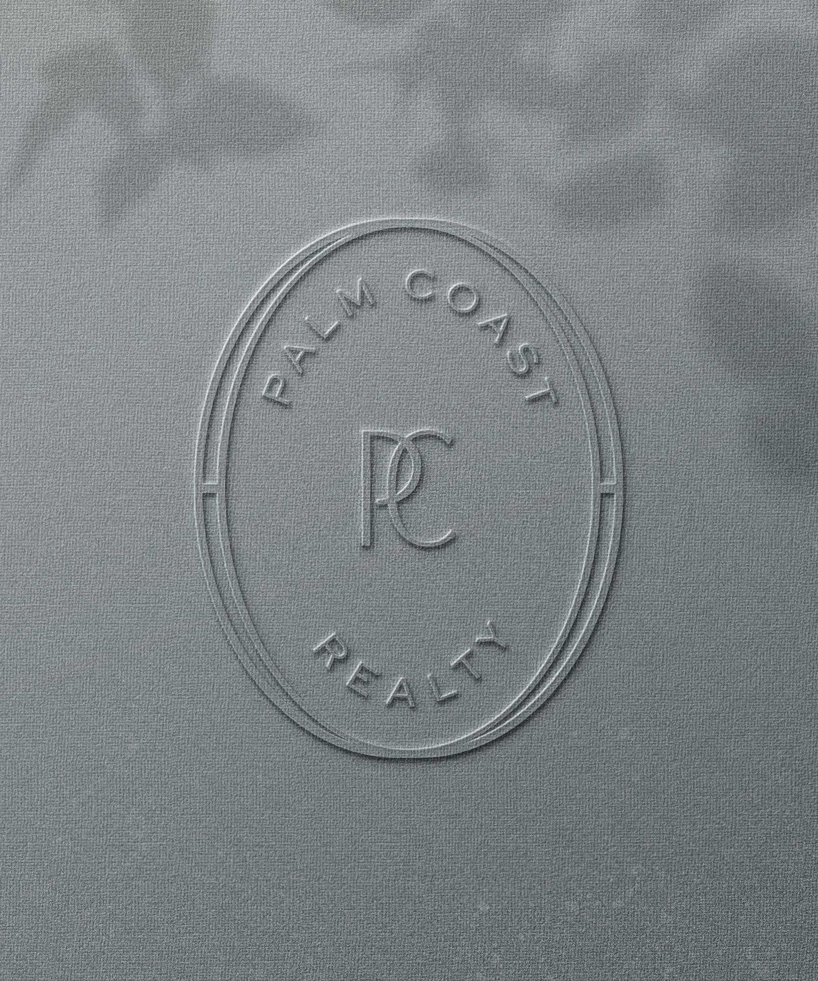 Close-up of embossed logo on light gray fabric with the words 'Palm Coast Realty' and a stylized 'pc' in the center.